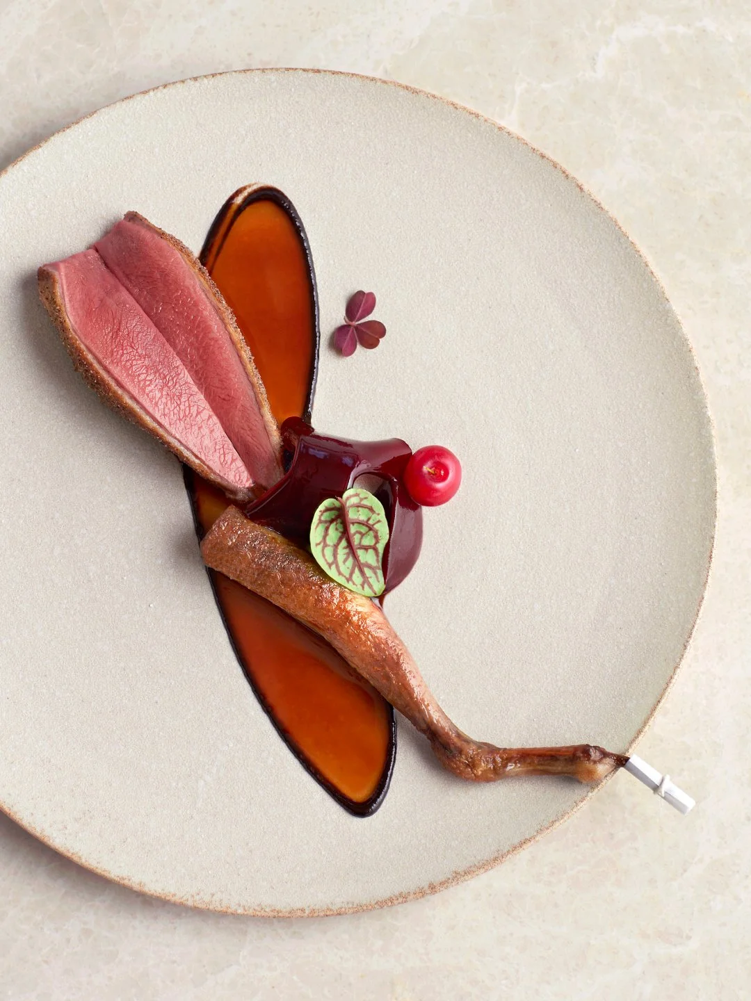 Elegant dessert designed as a butterfly on a white plate, featuring a duck breast, caramelized apple slices, fruit compote, and edible flowers.