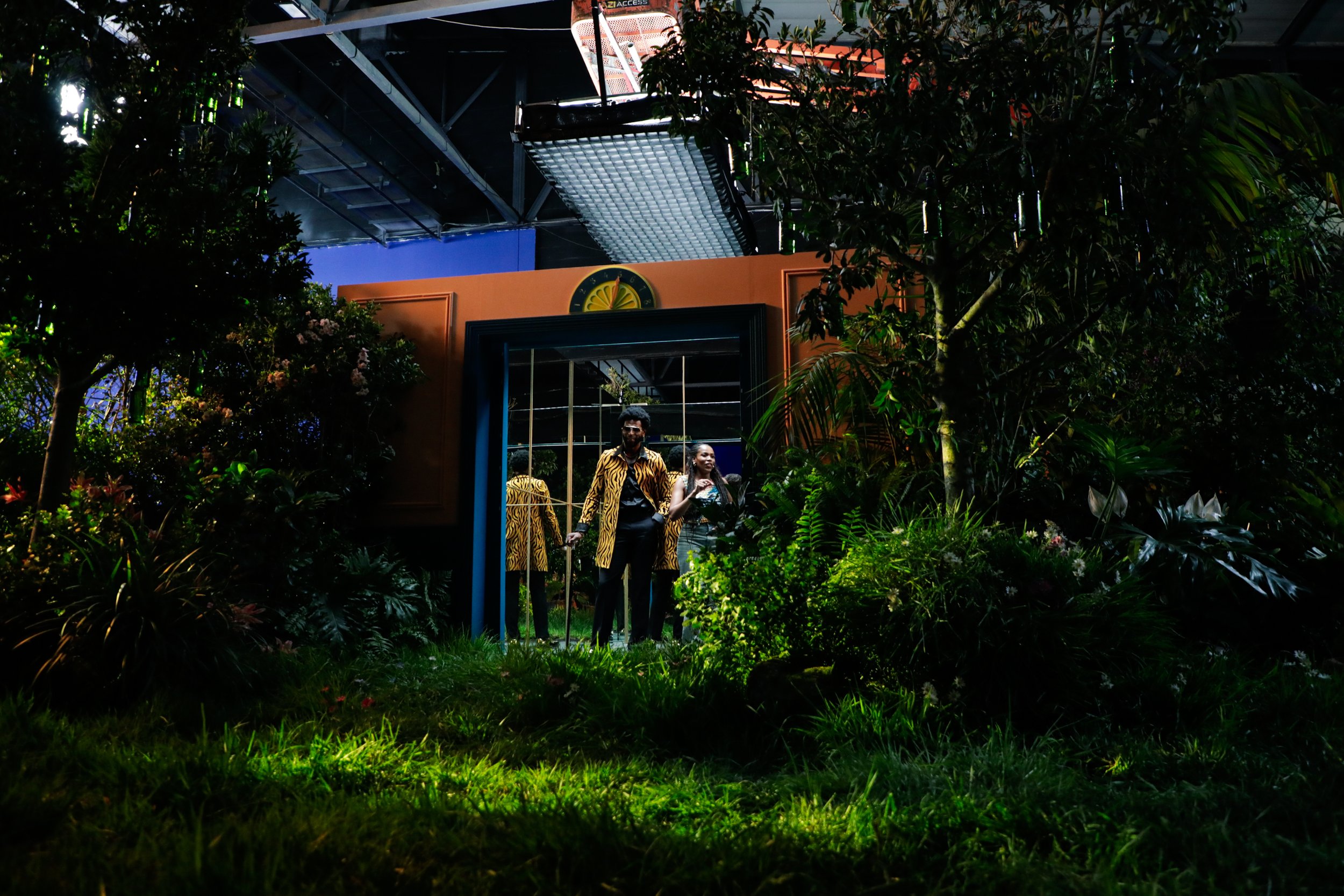 People entering a building through a mirror door surrounded by greenery and plants.