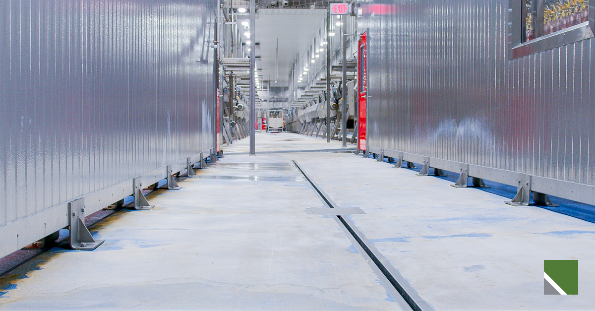 Industrial manufacturing facility aisle with machinery on both sides and a drain in the concrete floor.
