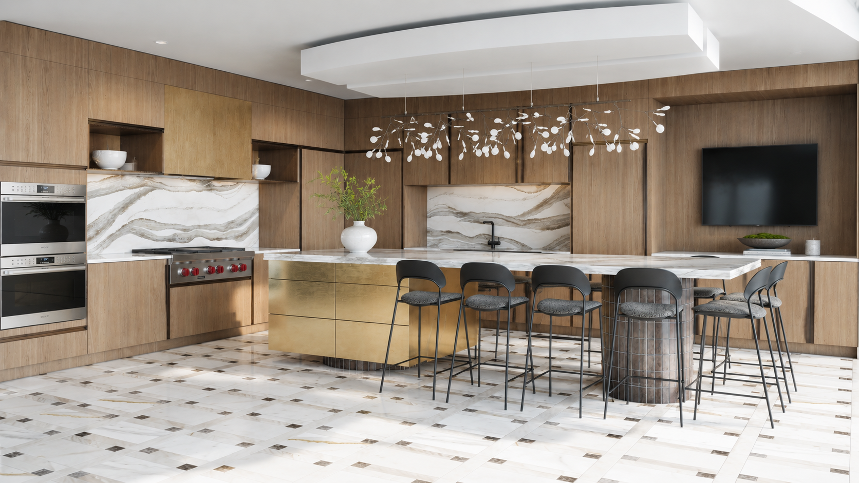 Modern kitchen with wood cabinetry and marble backsplash, gold island, black chairs, and a flat screen TV on the wall.