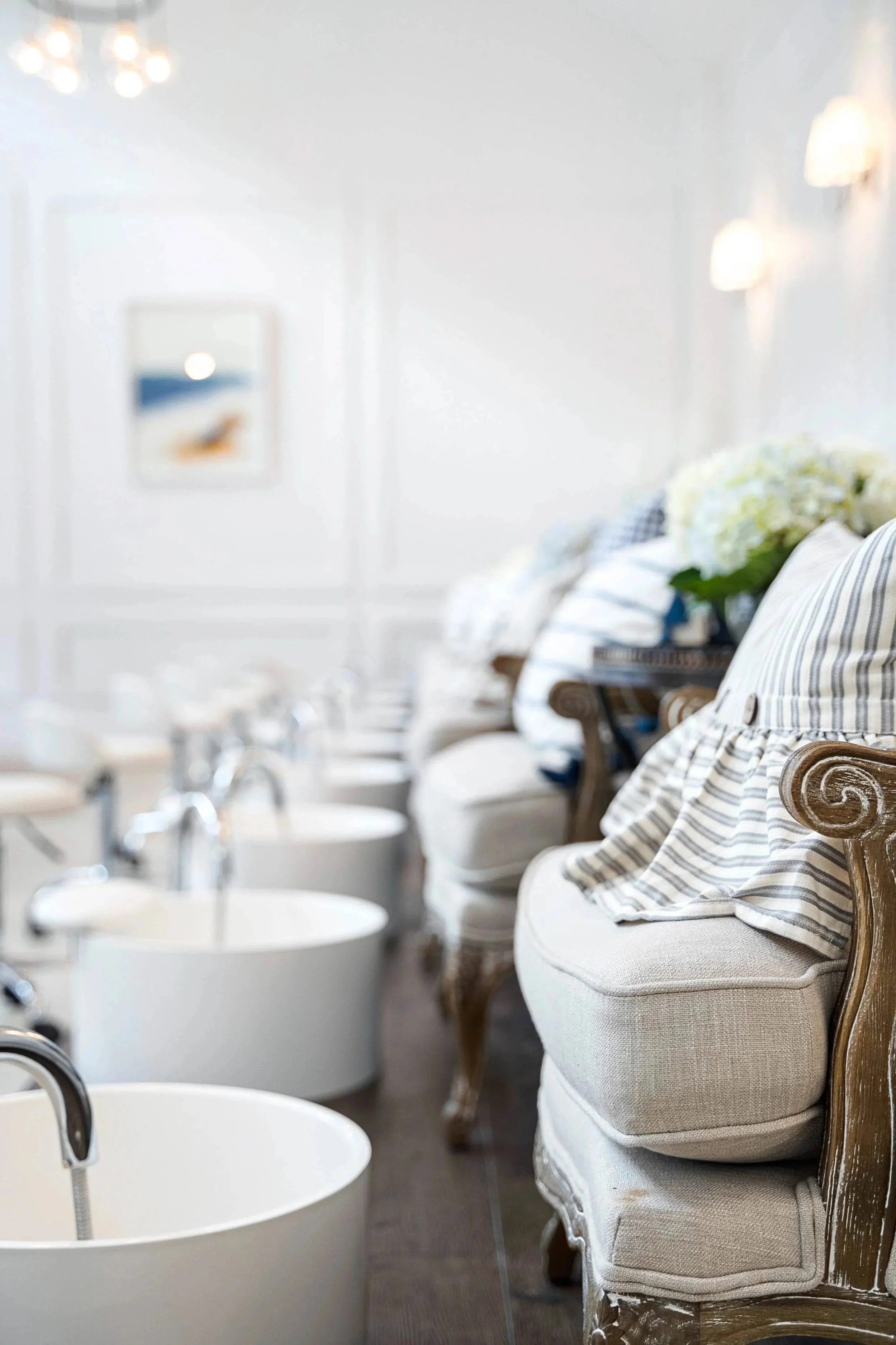 First, crisp white walls create a bright and clean salon. Then, elegant chairs and white pedicure tubs line the room, while a fresh bouquet of white flowers adds a soft, welcoming touch.