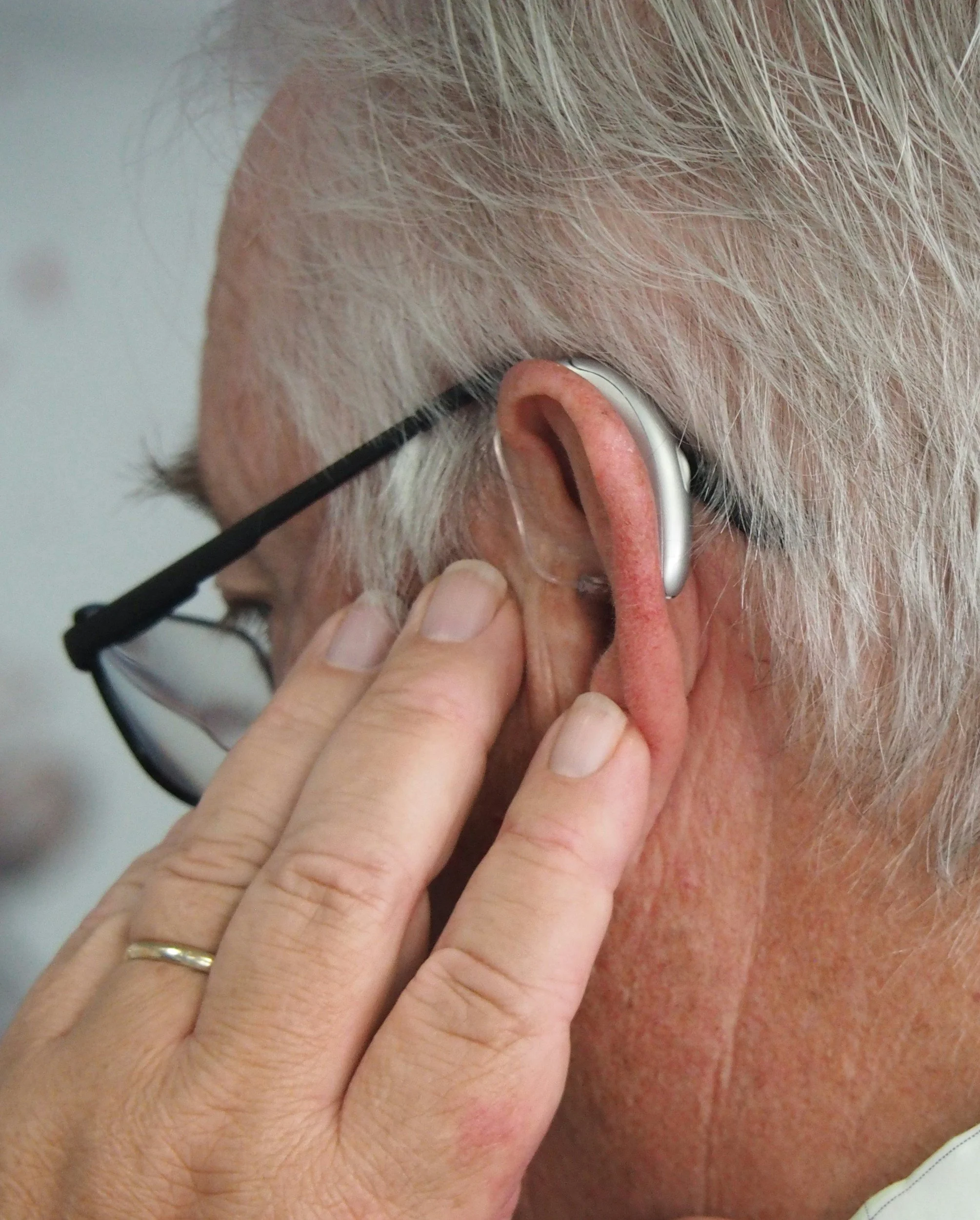 Older adult adjusting a hearing aid as part of hearing health support and hearing loss care