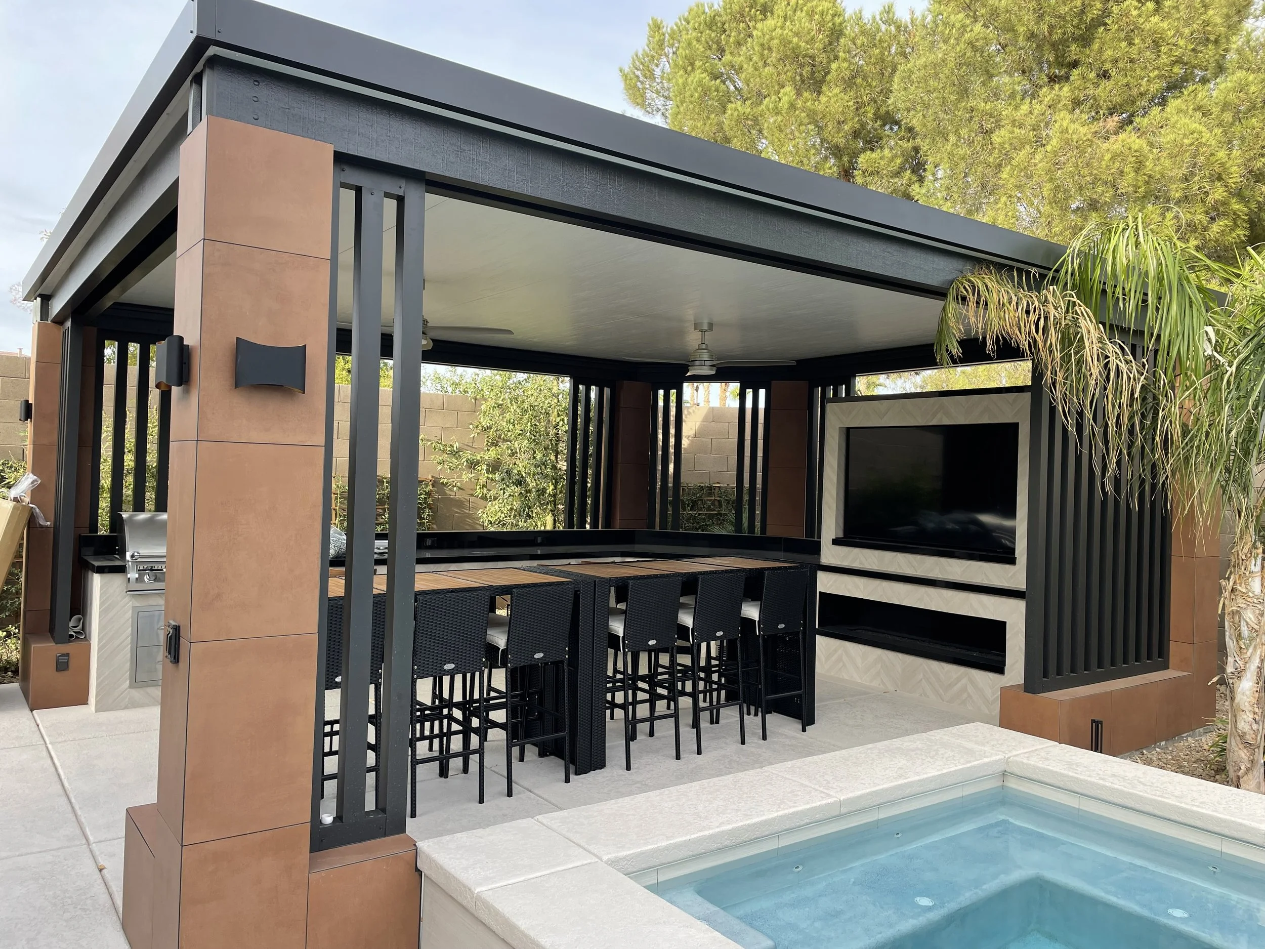 Modern outdoor patio with a pergola, dining area, TV, grill, and pool.