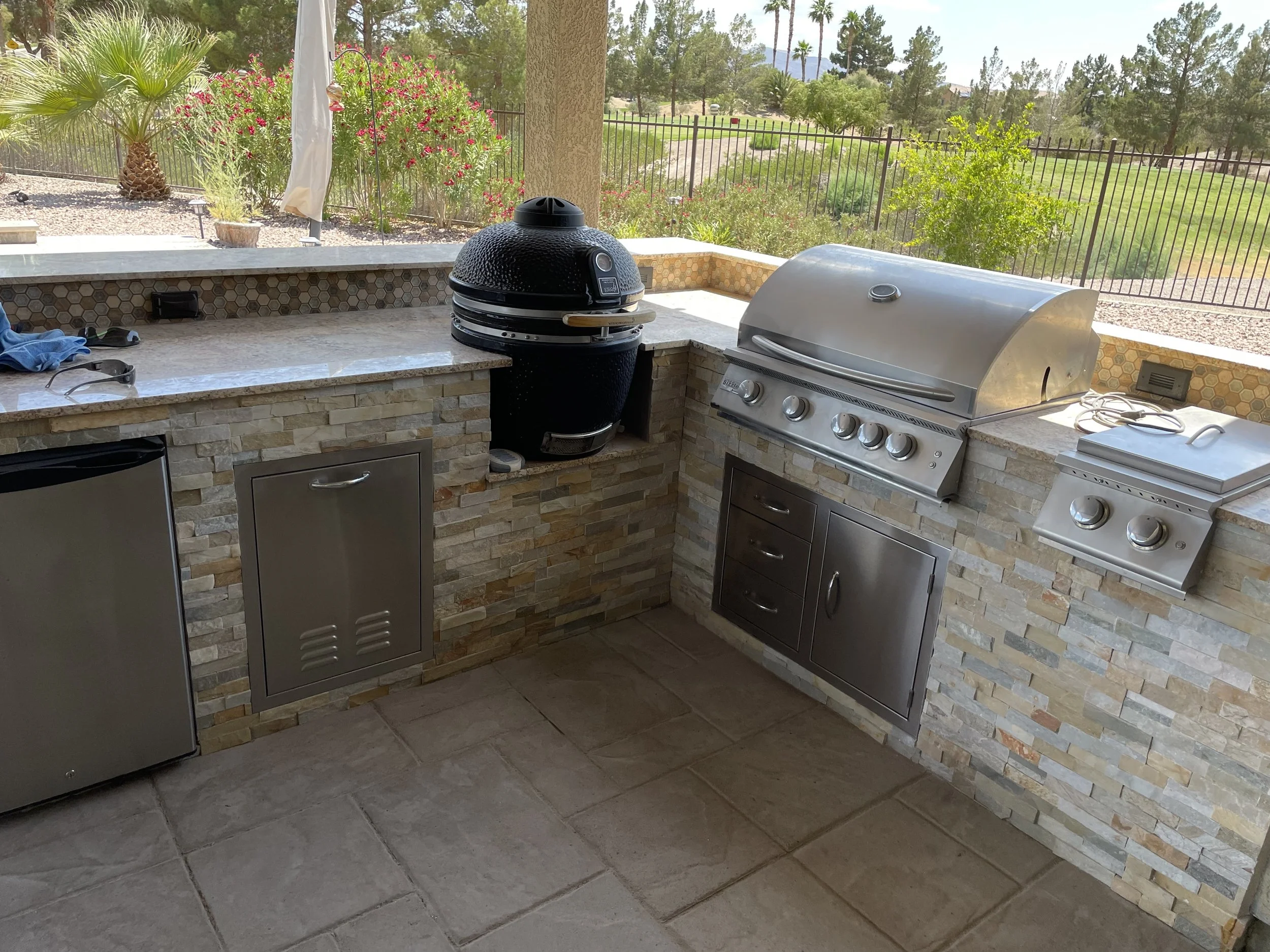 Outdoor kitchen with a grill, smoker, fridge, and stone counter.