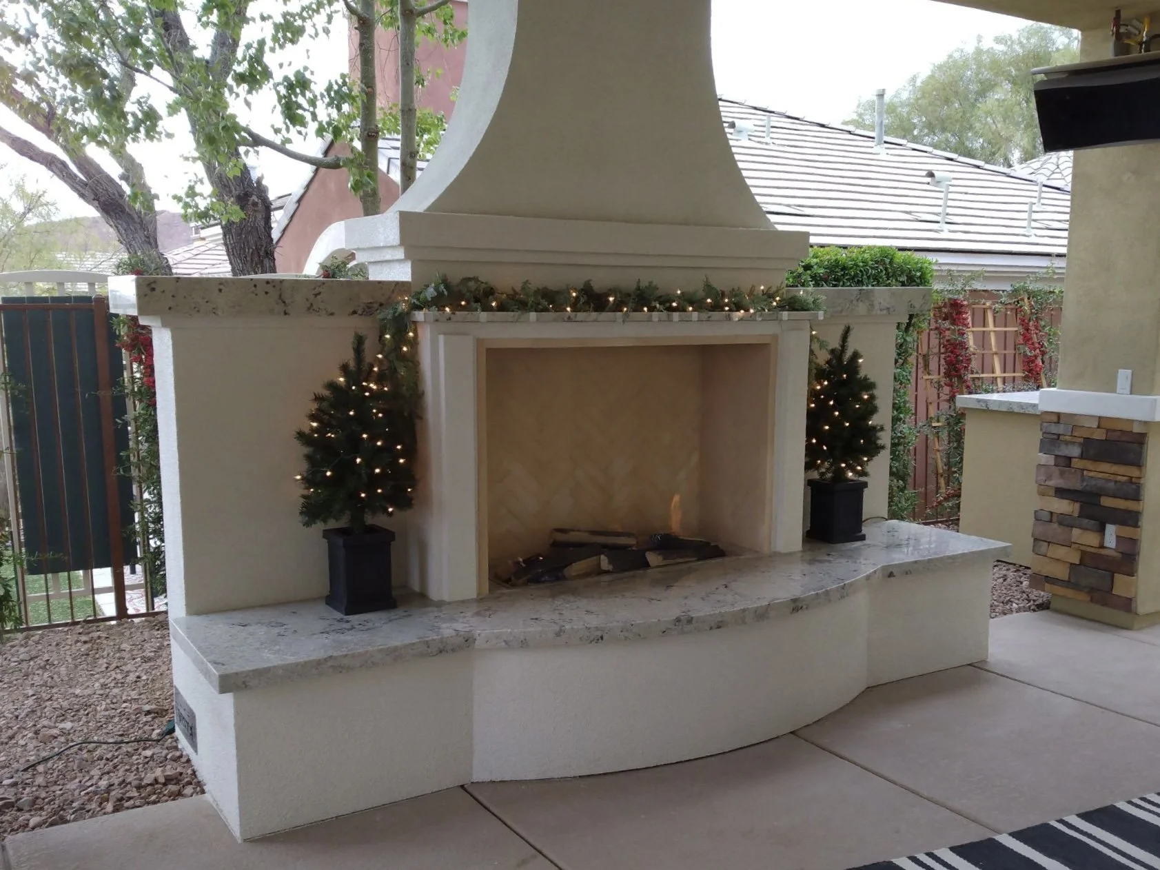 Outdoor fireplace with decorative Christmas trees and lights on a patio
