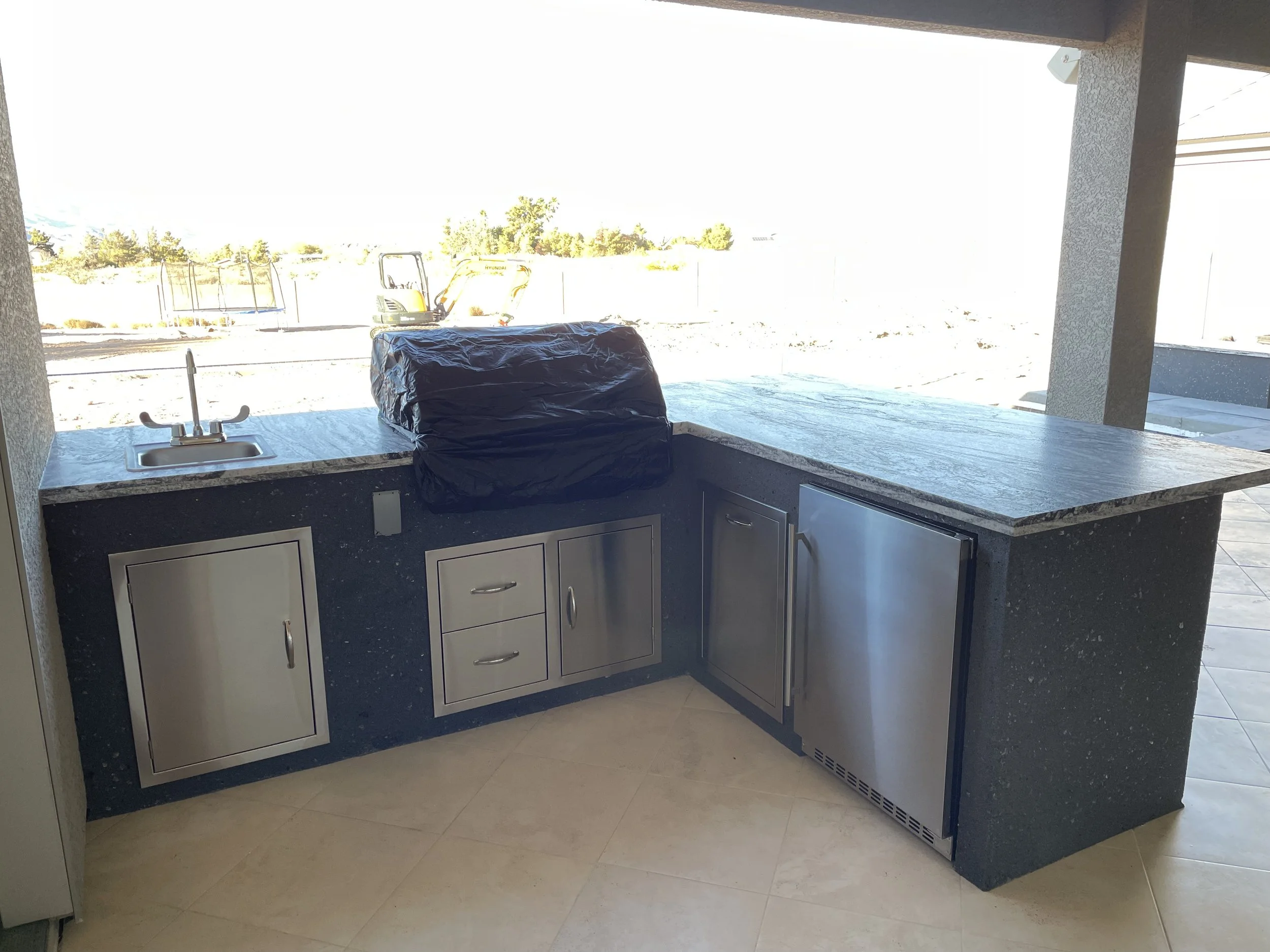 Outdoor kitchen with a sink, covered grill, stainless steel cabinets, and a refrigerator.