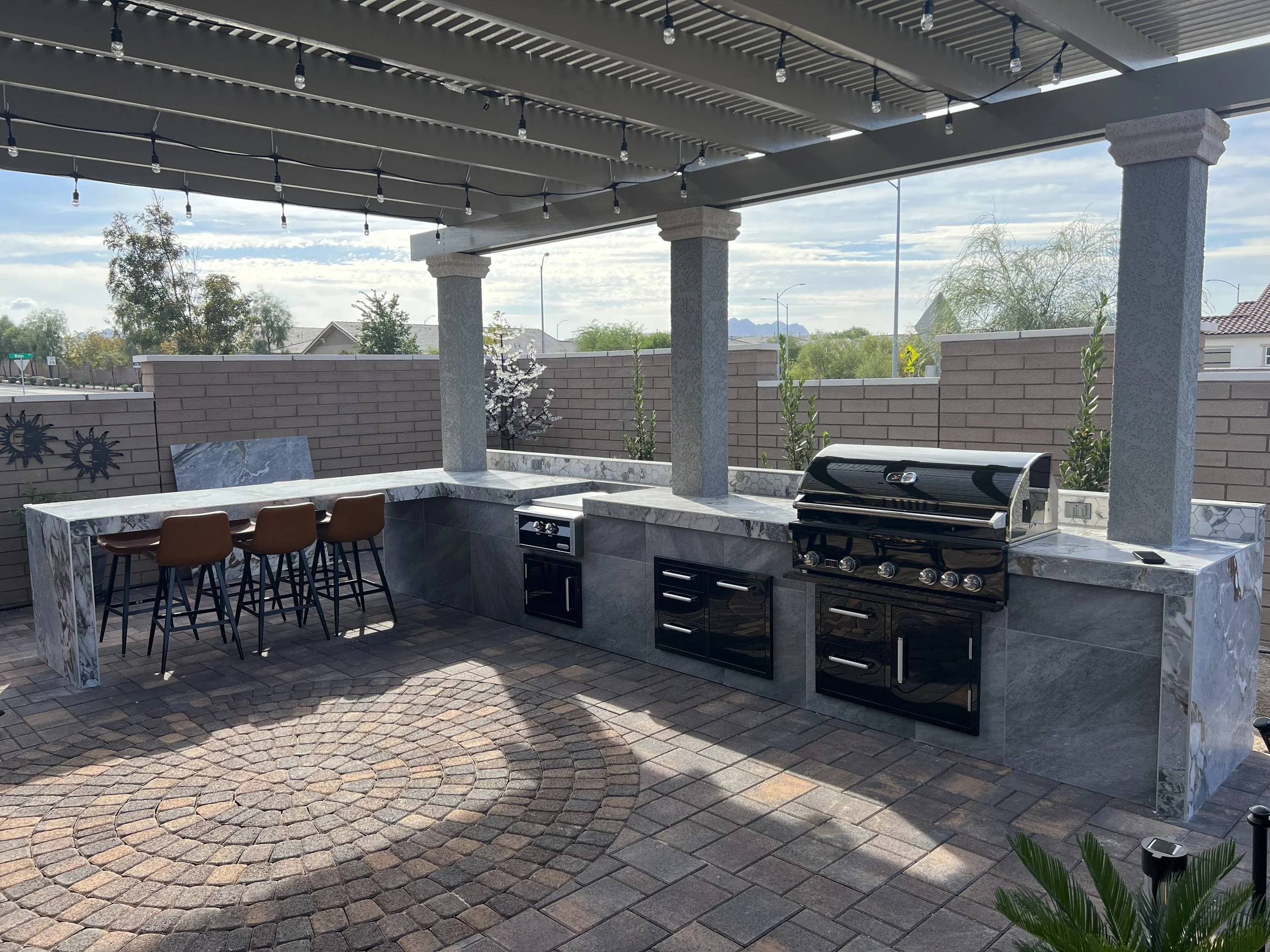 Outdoor kitchen with pergola, featuring a built-in grill and bar seating on a tiled patio.