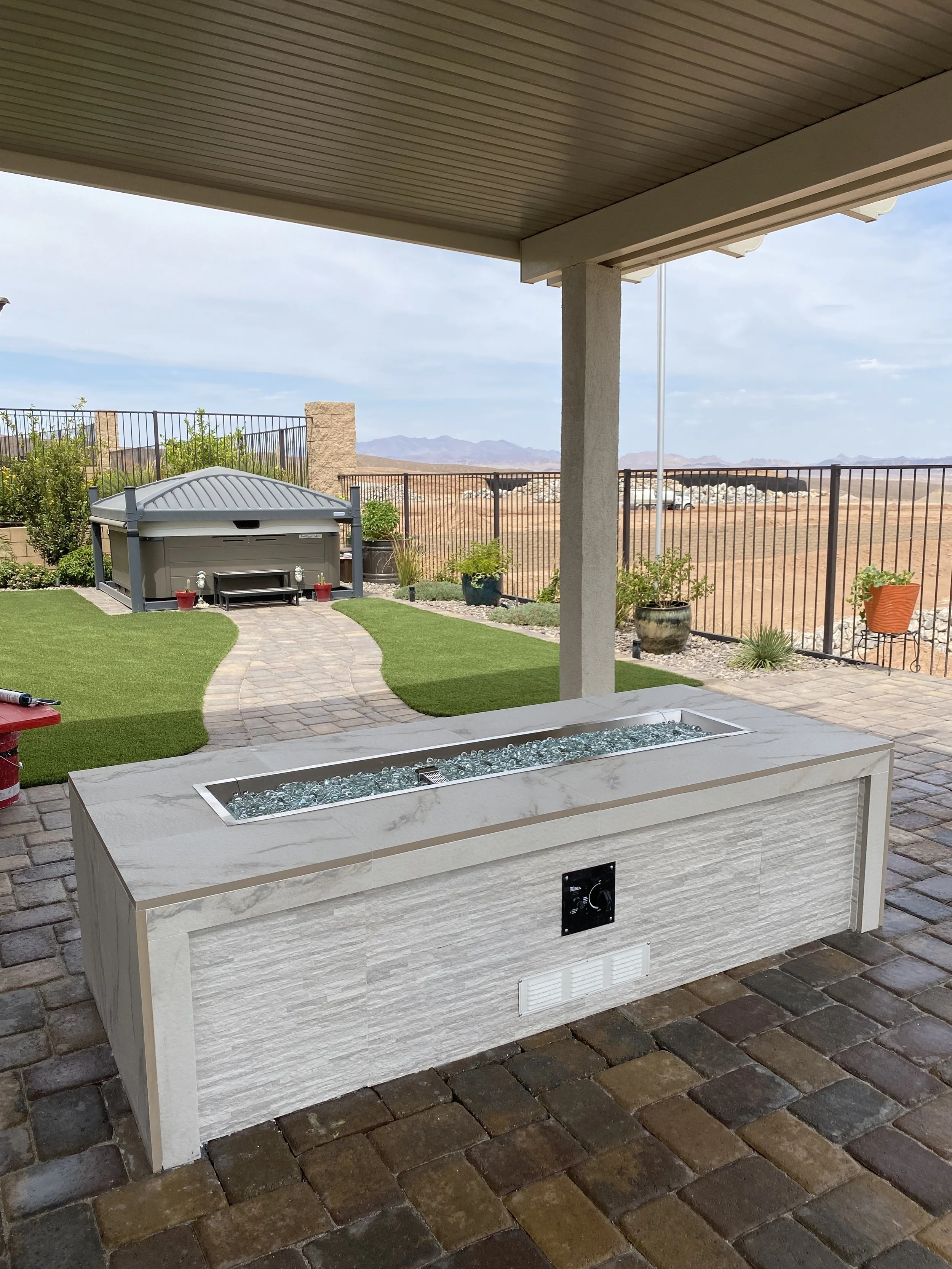 Backyard patio with a fire pit, artificial grass, and a hot tub