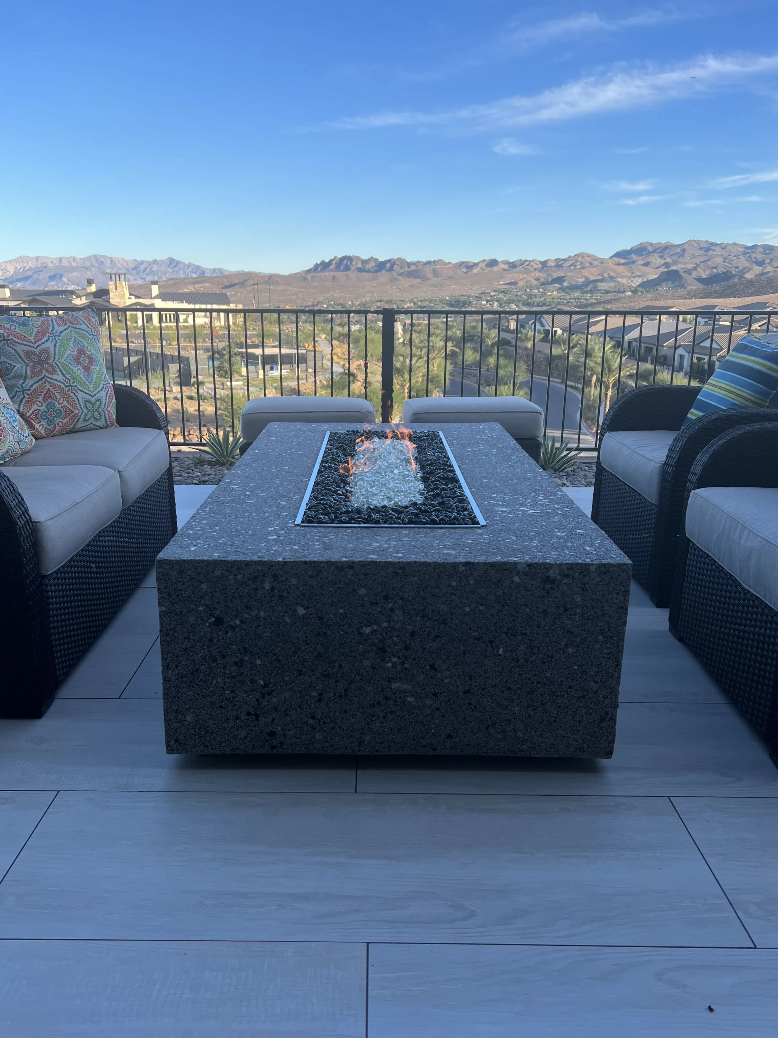 Patio with fire pit table surrounded by wicker seating, with mountain view in background.