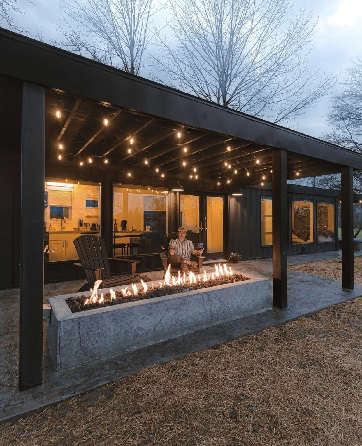 Modern outdoor patio with fire pit and string lights, person seated, evening setting