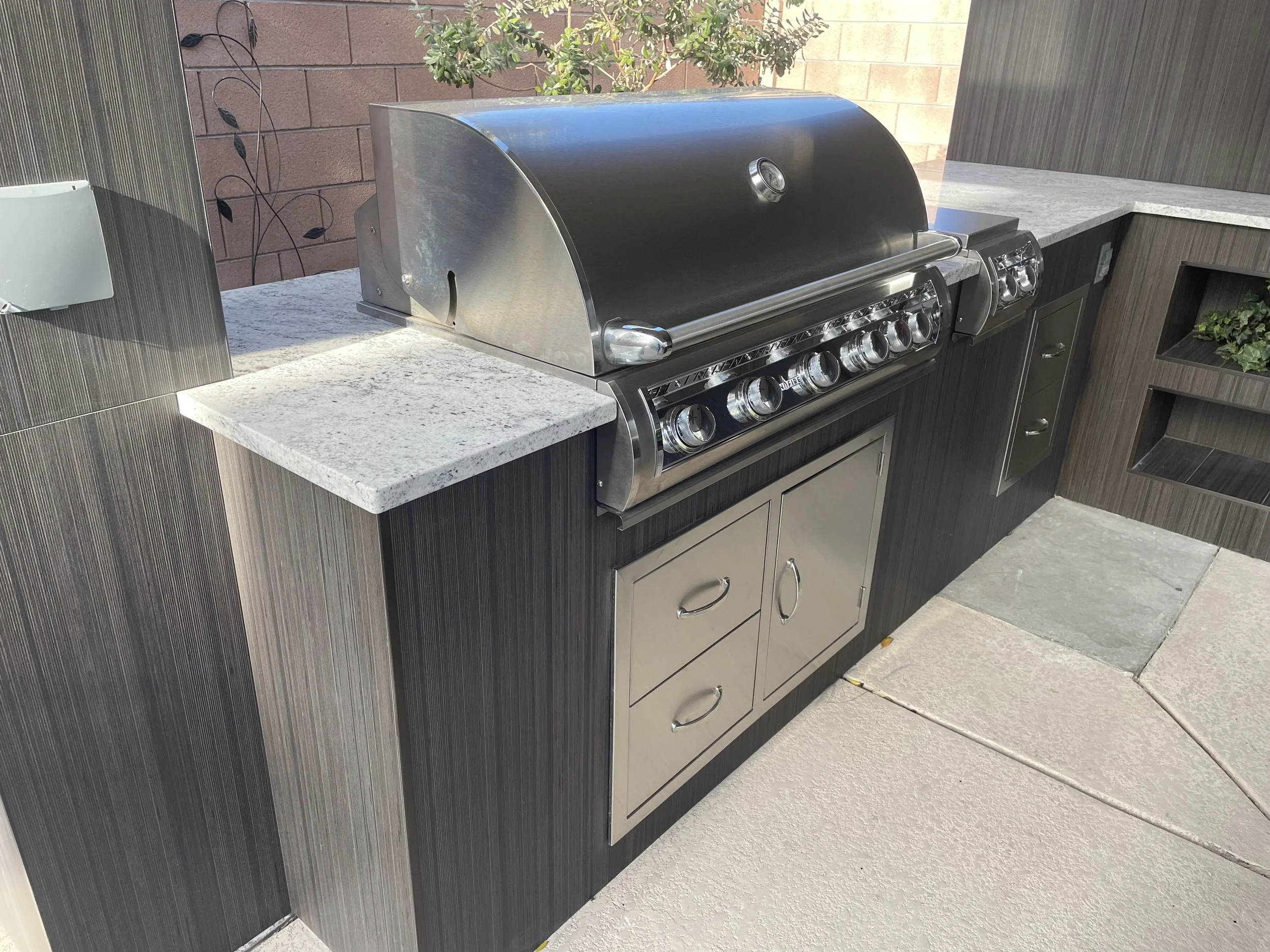 Outdoor built-in gas grill with stainless steel surfaces and cabinetry in a modern outdoor kitchen setup.