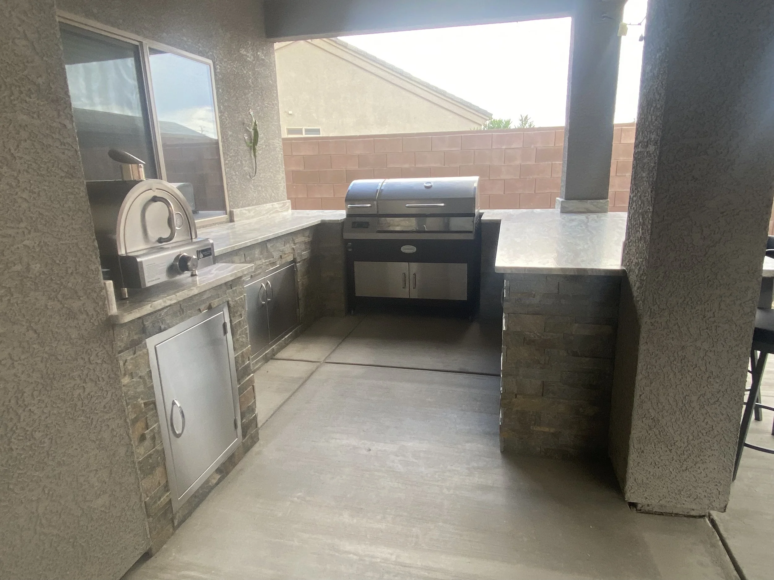 Outdoor kitchen with a pizza oven and a grill on a stone countertop.