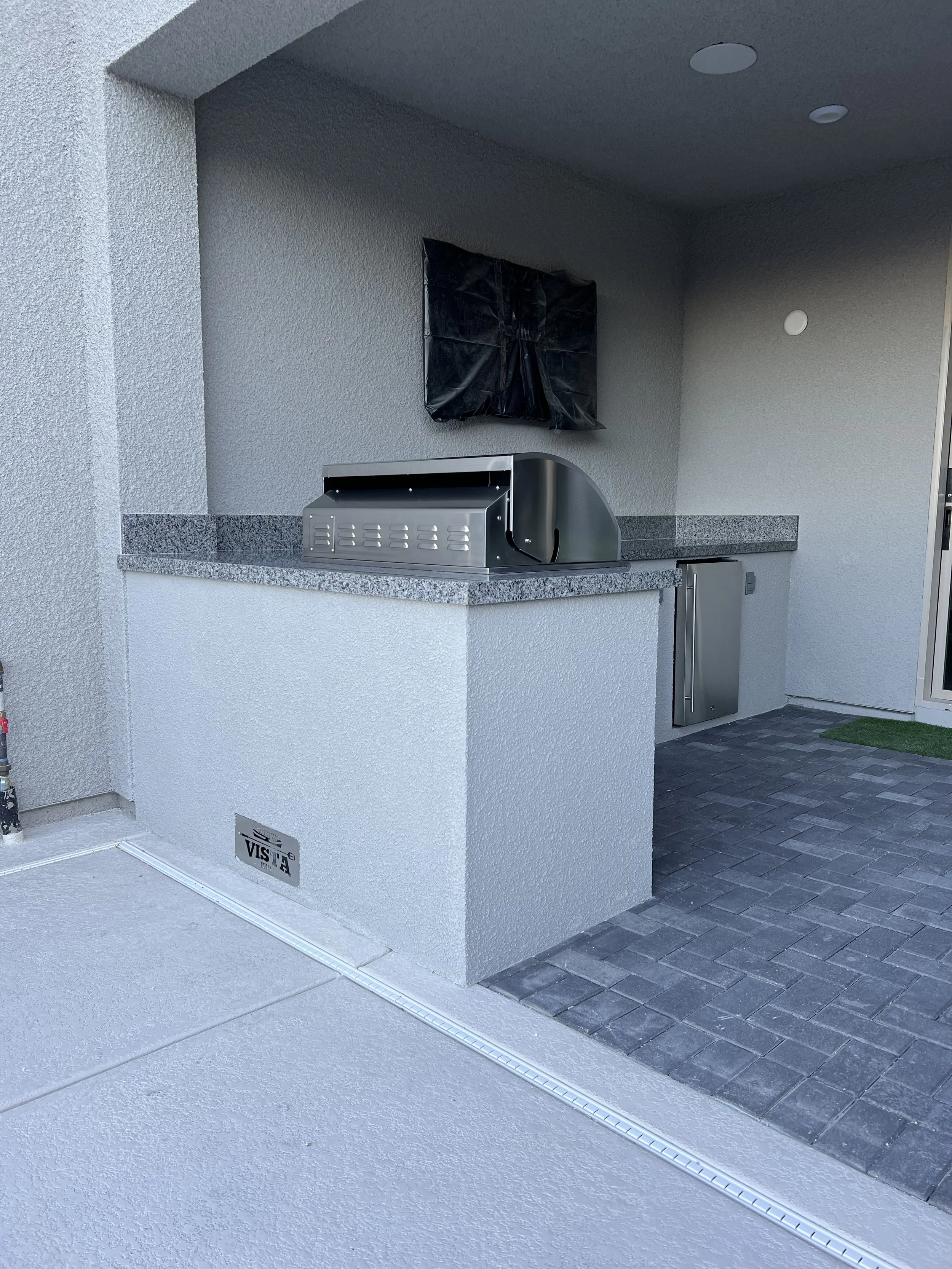 Outdoor kitchen area with built-in grill, granite countertop, and a covered fixture on the wall.