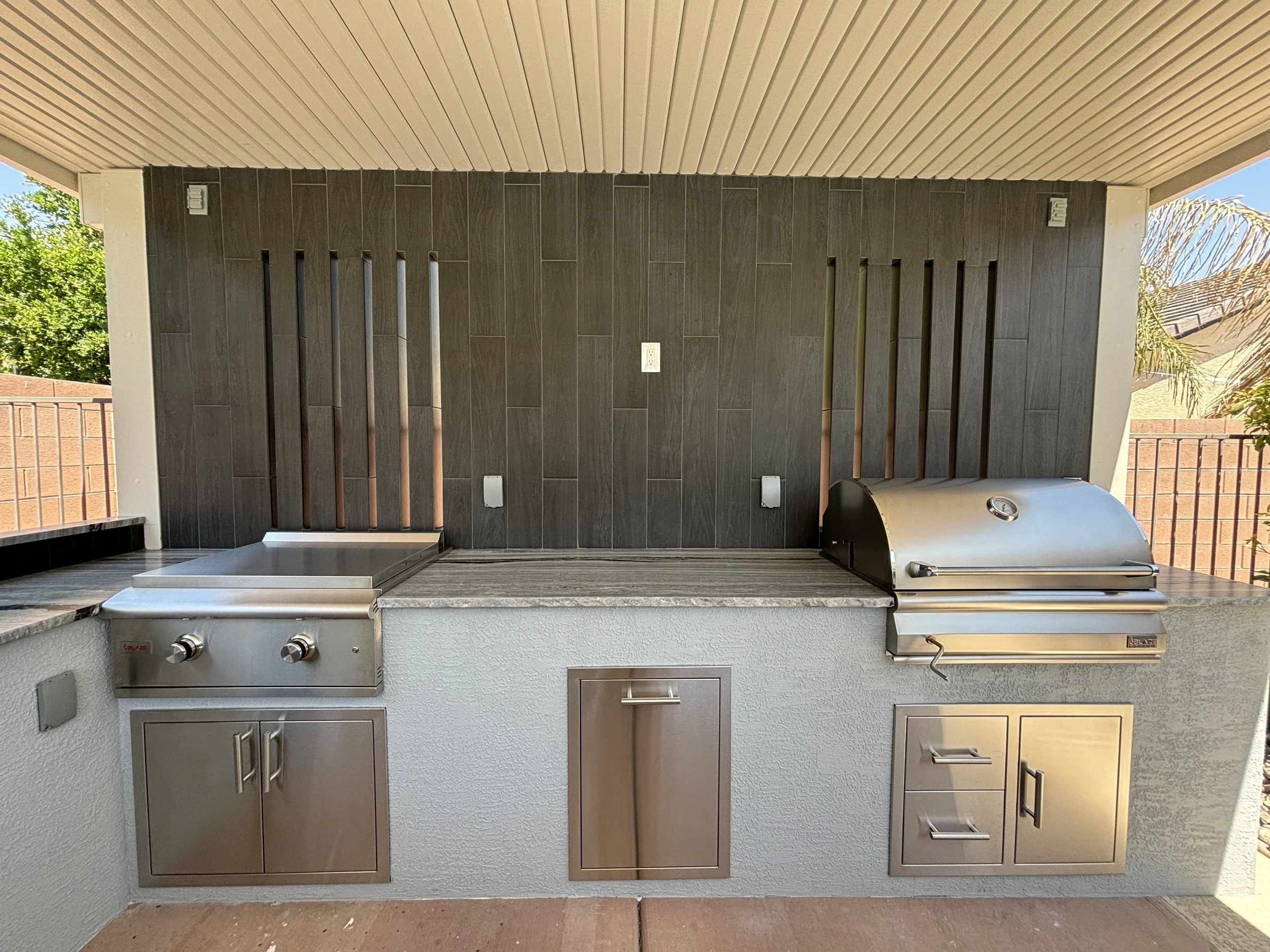 Outdoor kitchen with stainless steel grill and cabinetry under a covered patio.