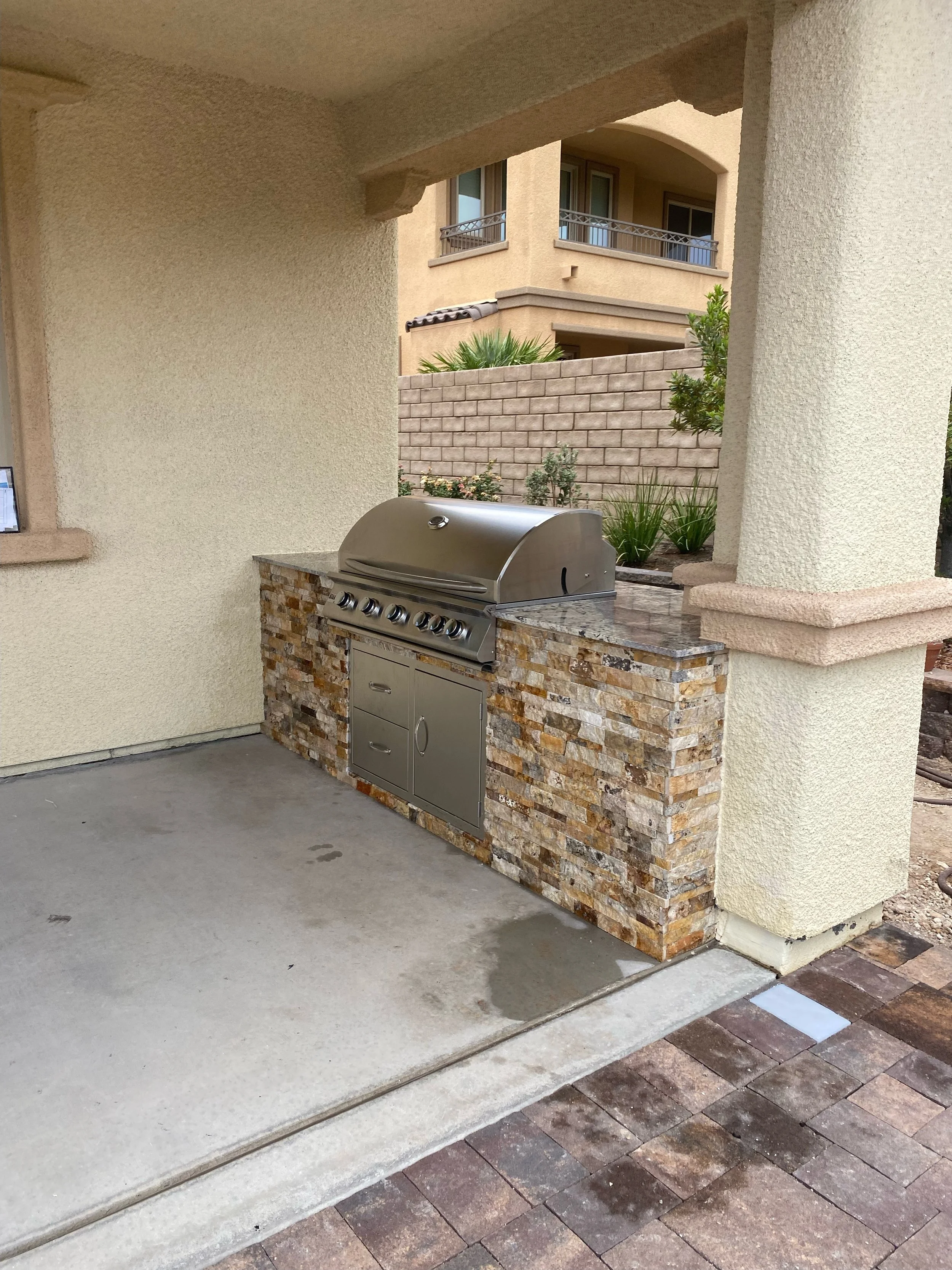 Outdoor built-in barbecue grill with stone veneer surround on a covered patio.