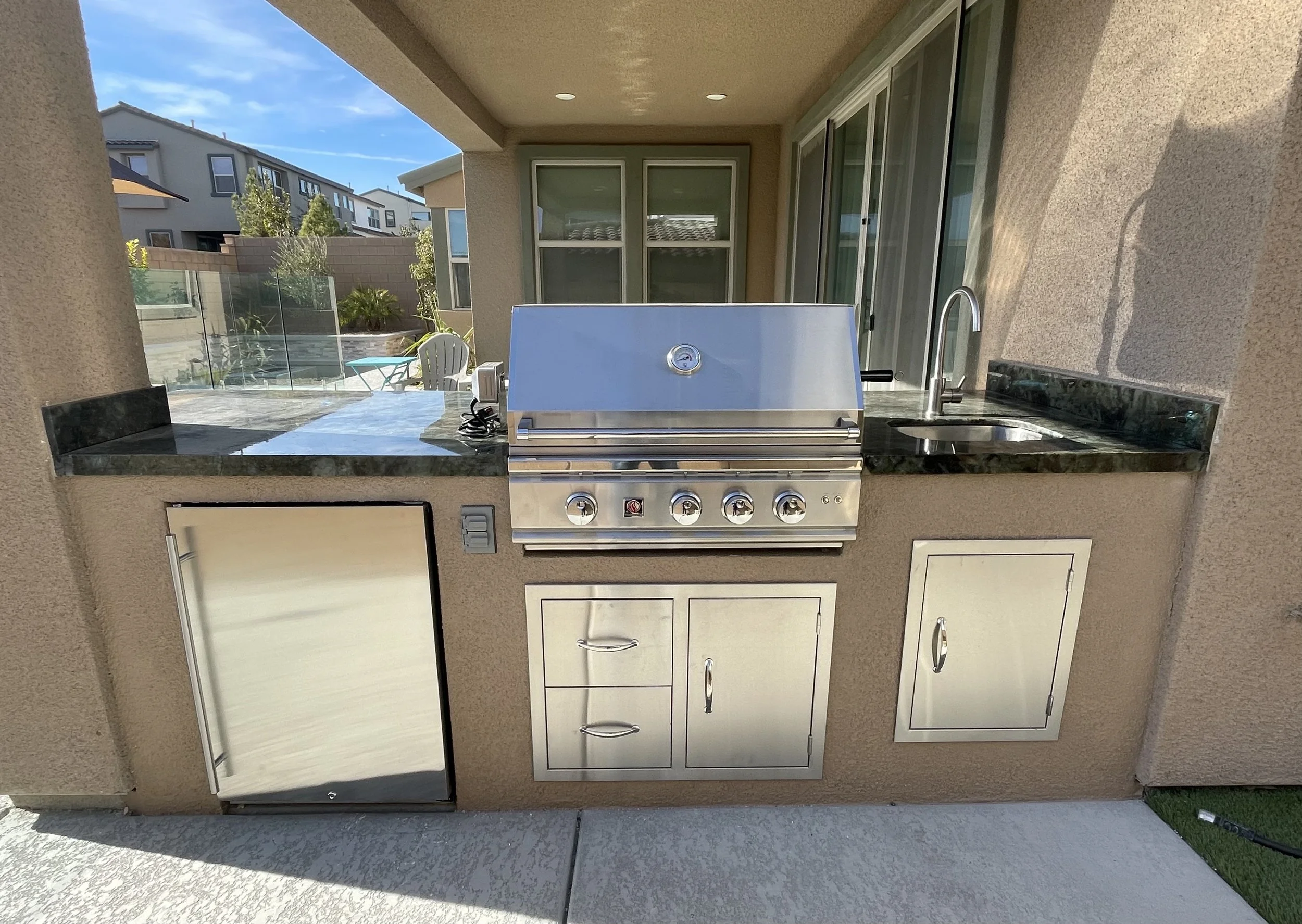 Outdoor kitchen with built-in stainless steel grill, refrigerator, sink, and storage cabinets.