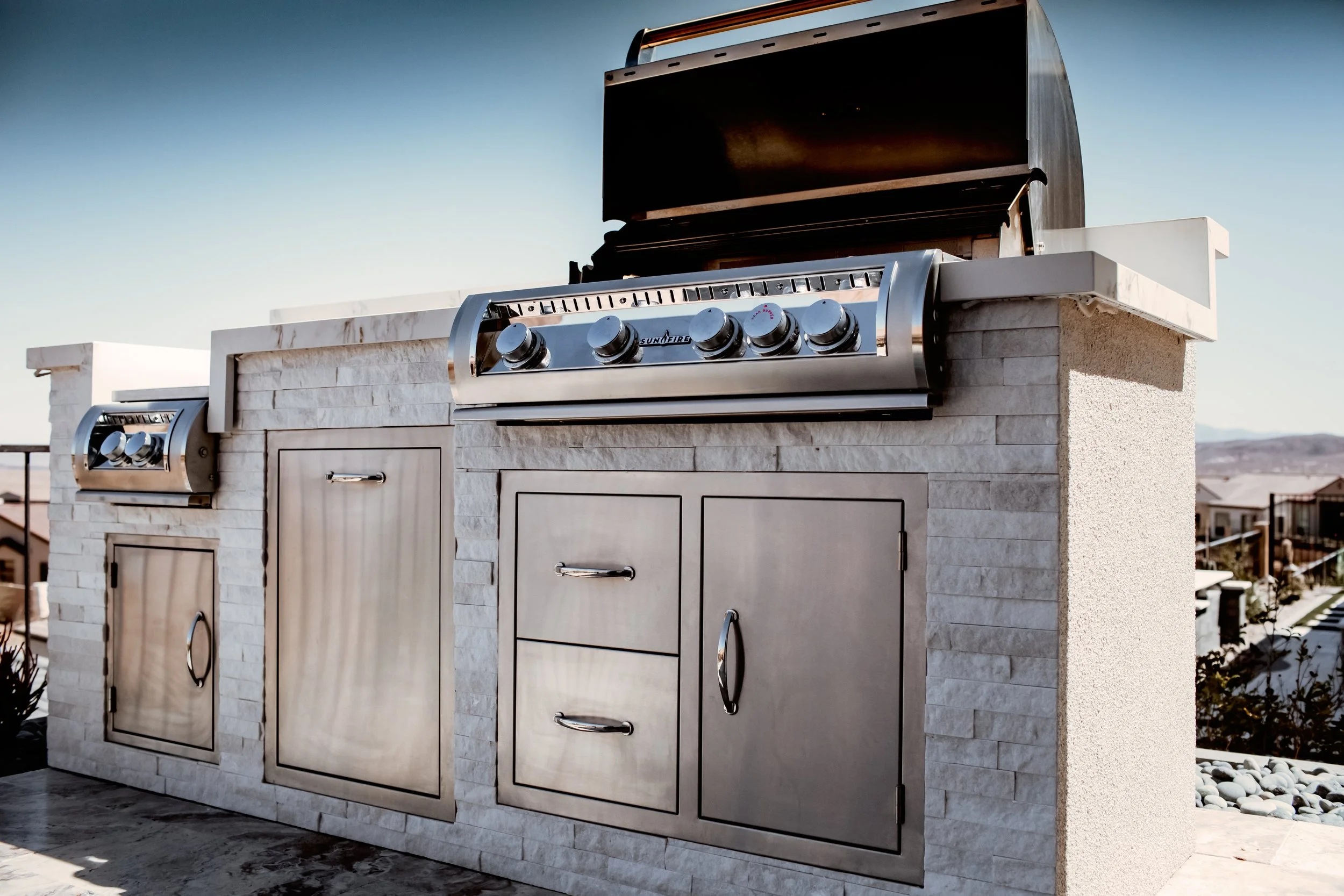 Outdoor stainless steel grill with storage cabinets and countertop in a modern patio setting.