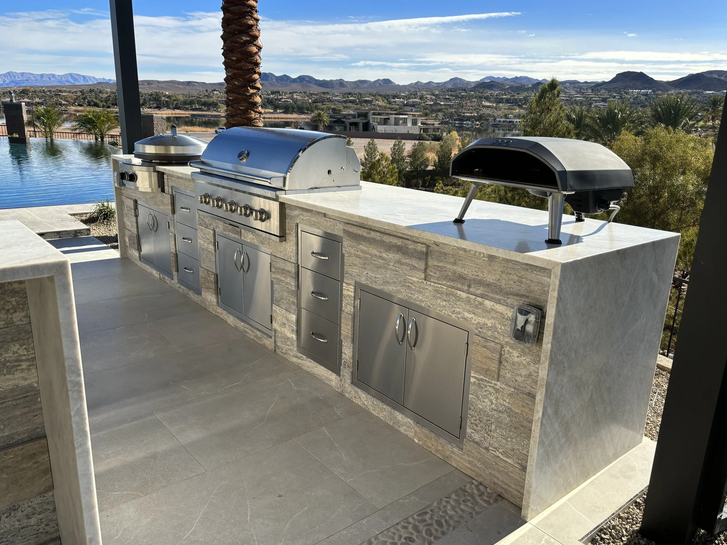 Outdoor kitchen with grill and pizza oven next to a pool with mountain views.