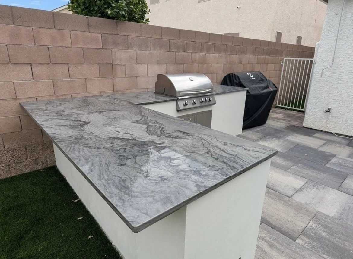 Outdoor kitchen area with stone countertop, stainless steel grill, and brick wall background.