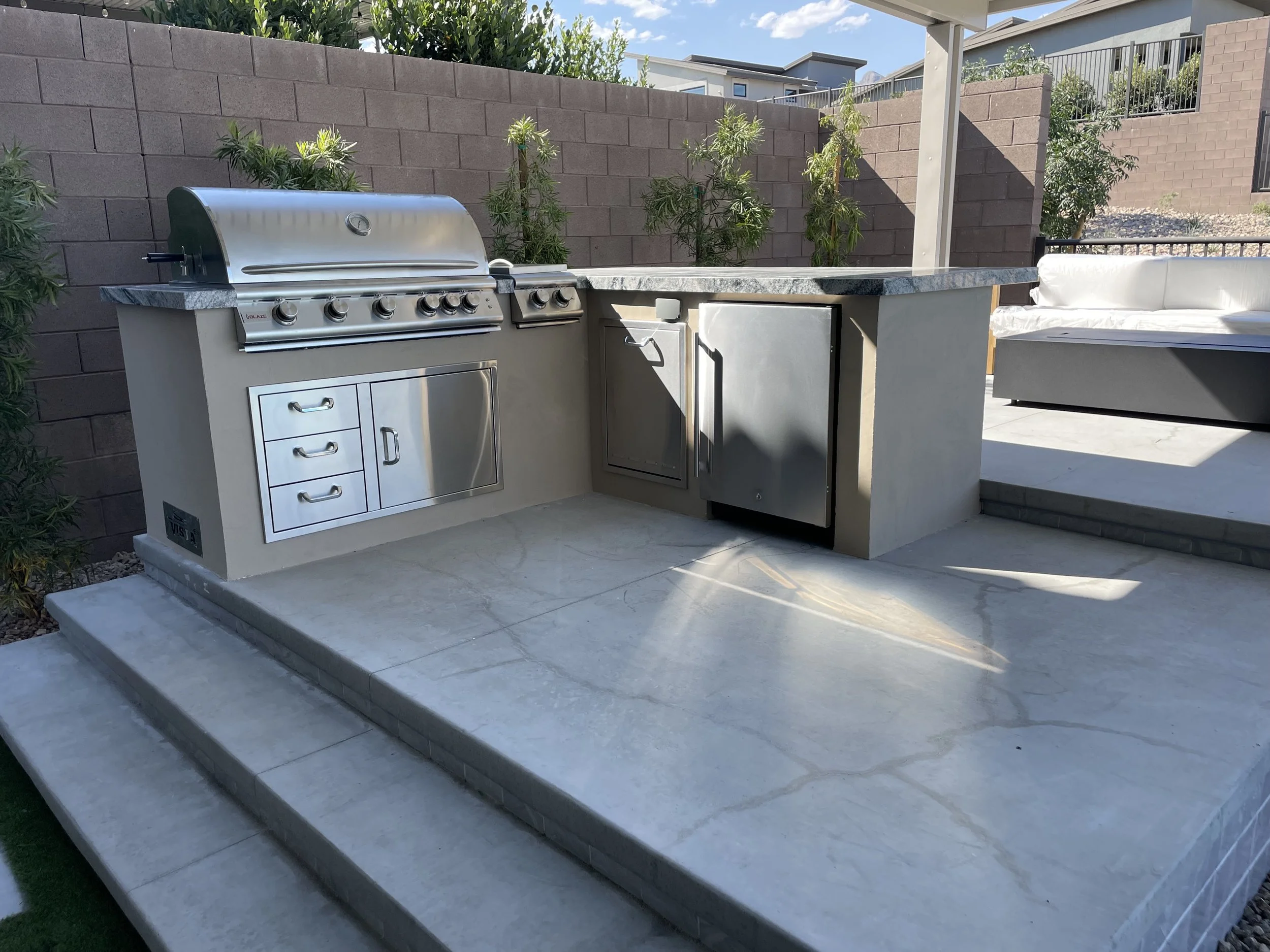 Outdoor kitchen with stainless steel grill, cabinets, and countertop on a patio.