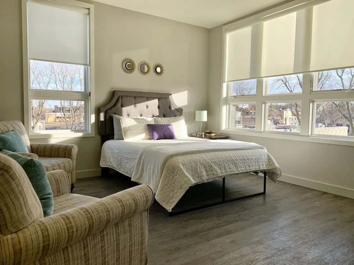 A large room with queen bed, extra seating, and natural light.