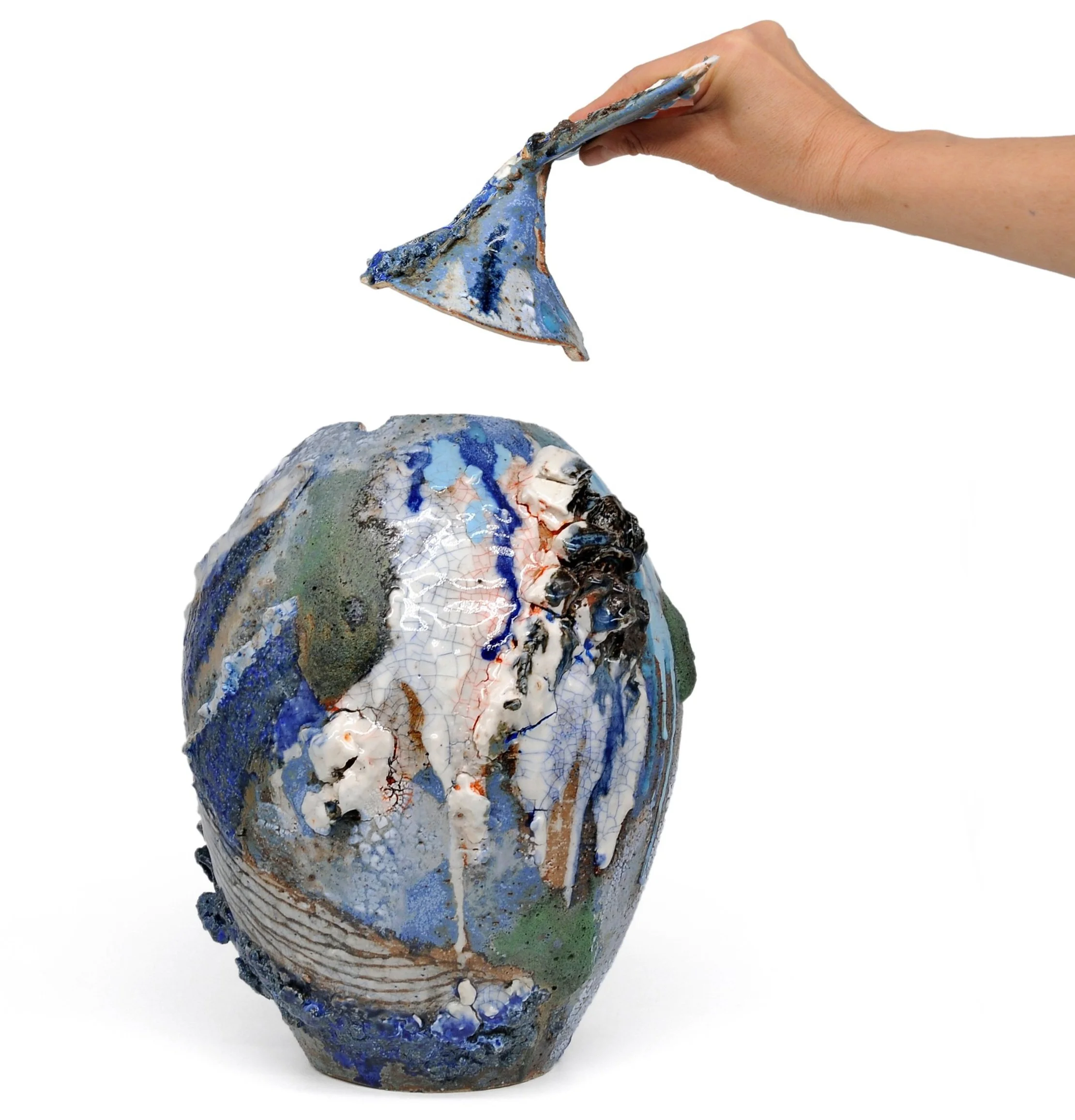 Hand lifting the lid of a unique, colorful ceramic vase with abstract designs.