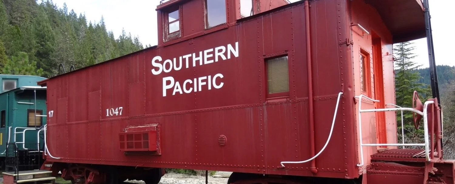 Red Southern Pacific caboose #17 with stairs and  woods in the background. Caboose next door.
