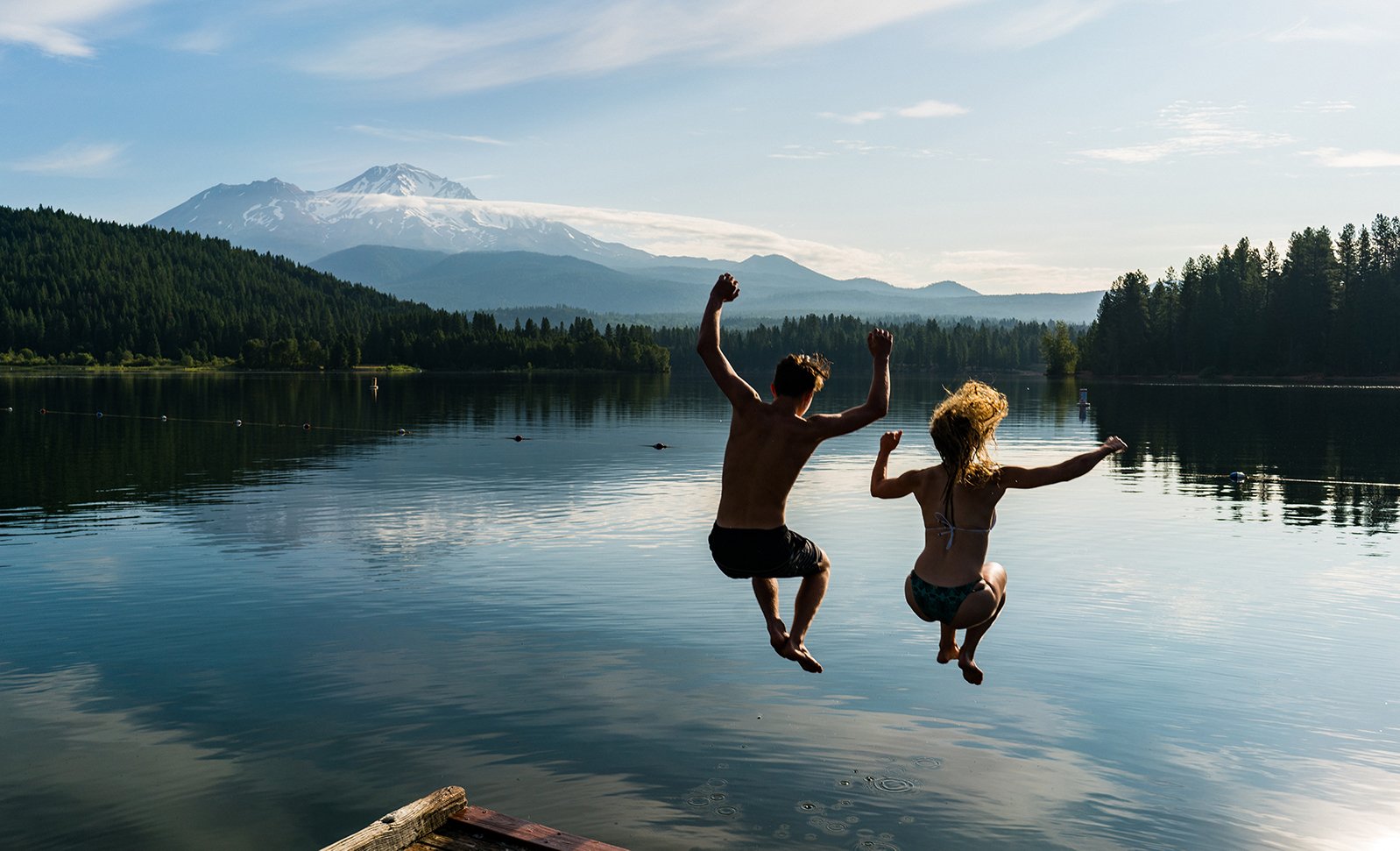 A man and woman jump into Lake Siskiyou with Mt. Shasta in the background