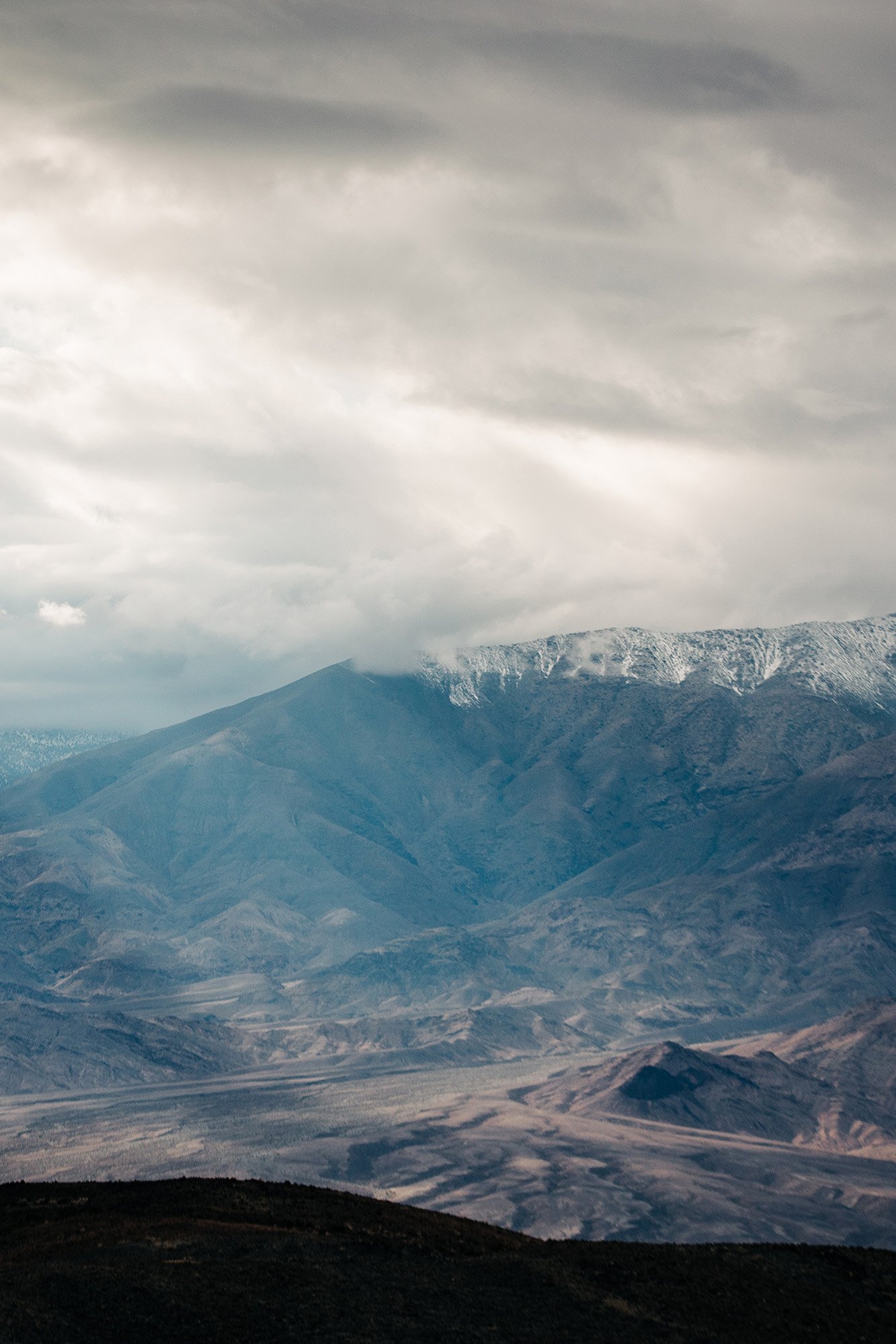 A view of Telescope Peak in Death Valley with sun shining down through a cloudy sky.