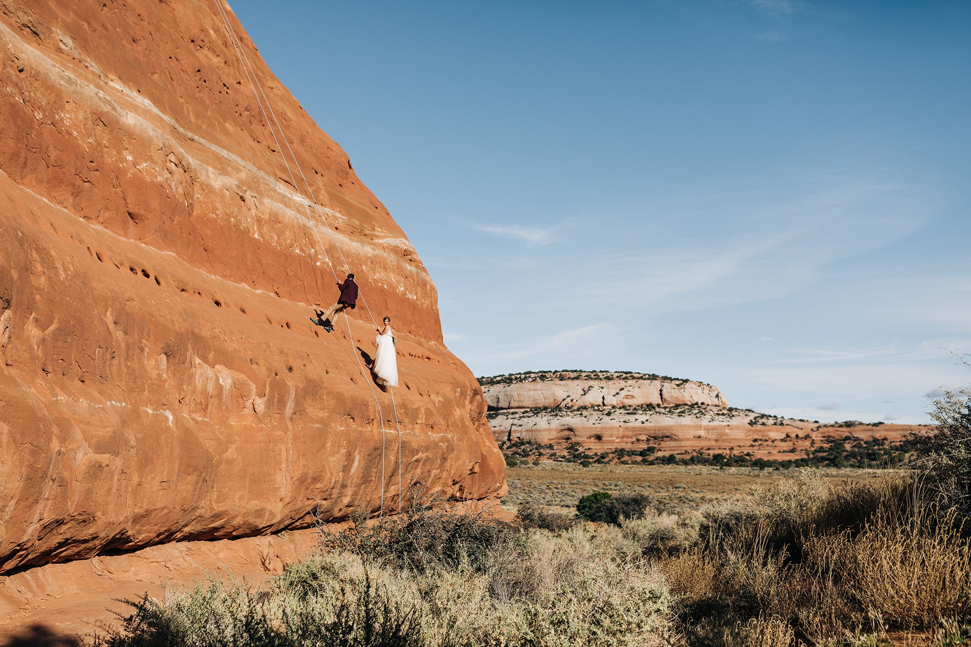 A couple climbs together with views of orange sandstone.