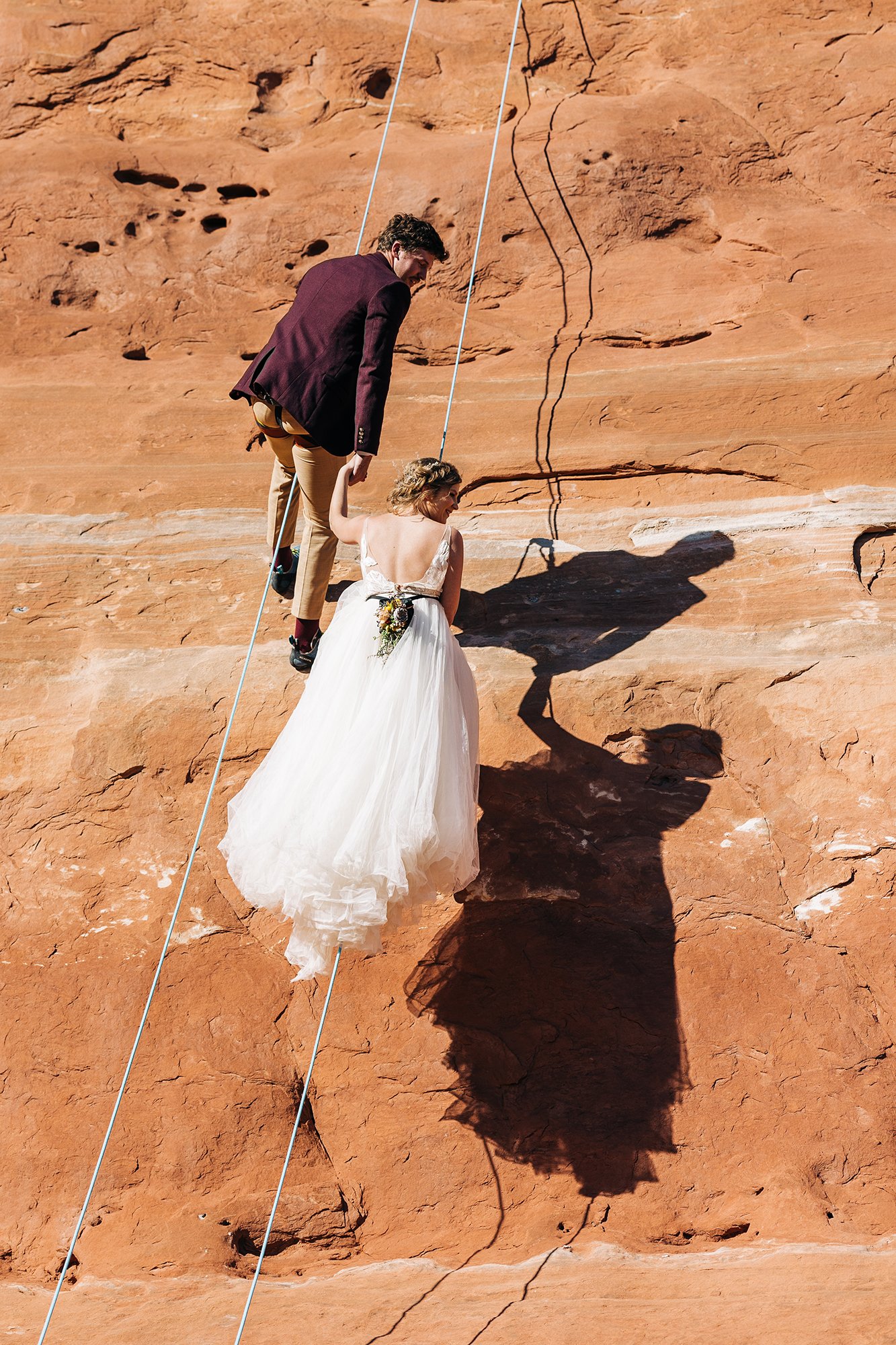A couple rock climbs in wedding attire in Moab. 