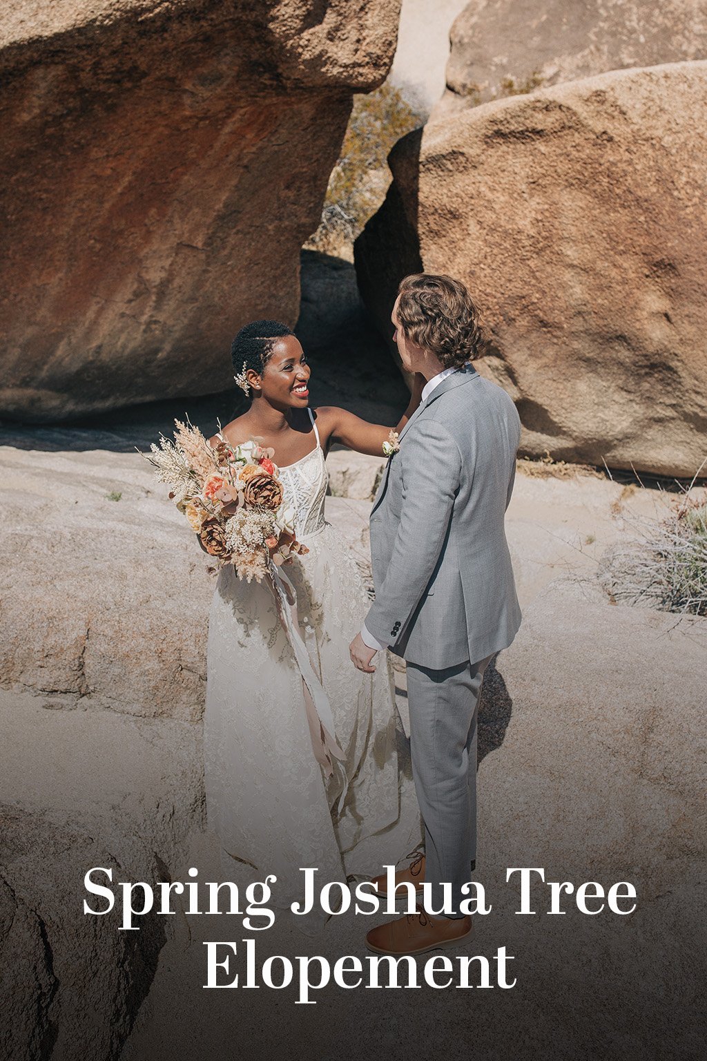 A married couple stands together in front of granite rocks with text reading "Spring Joshua Tree Elopement".