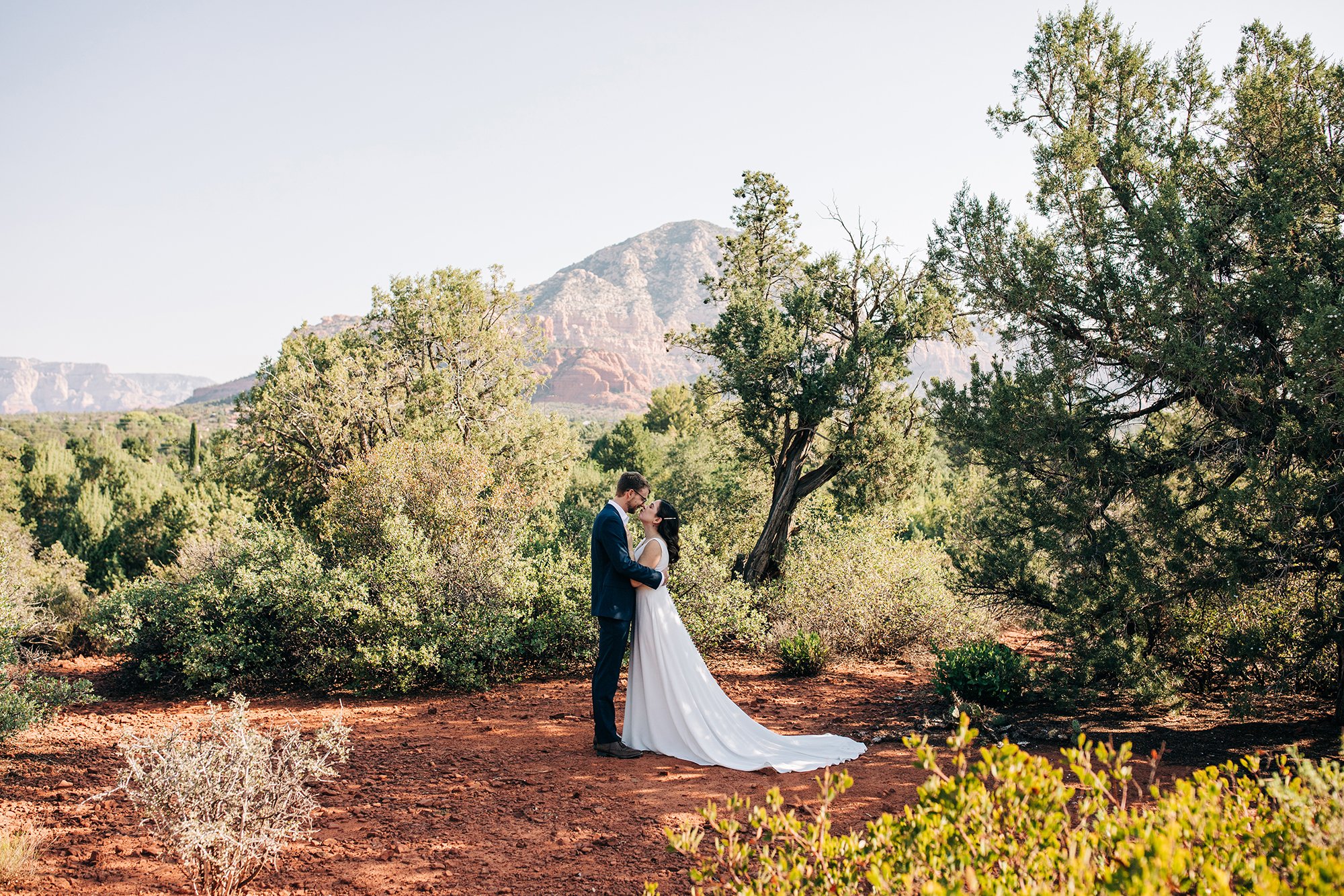 Stephanie and Matthew embrace on their wedding day amongst trees and red rocks. 