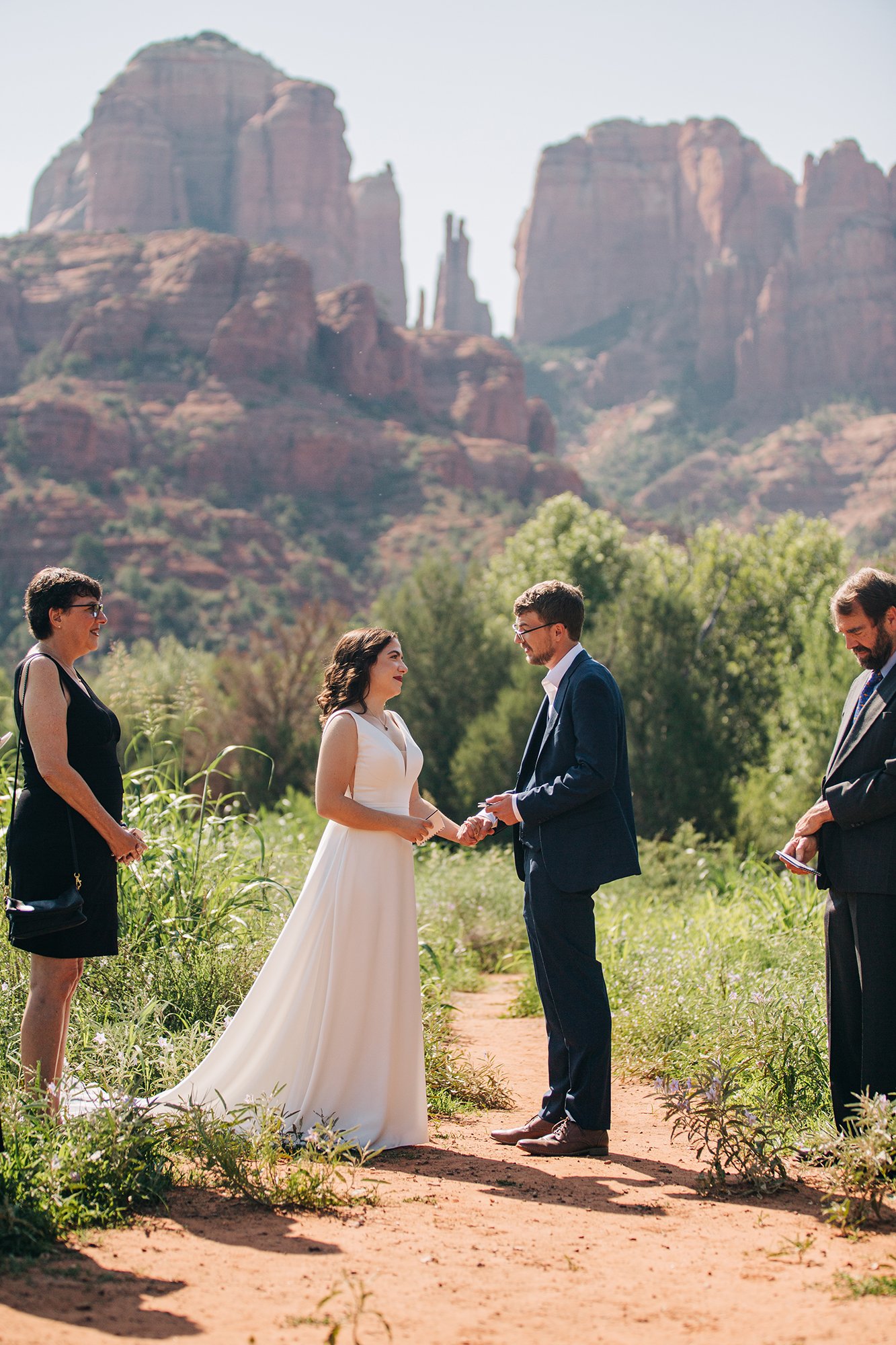 Stephanie, dressed in a long white wedding dress, looks lovingly at her groom, Matthew during this outdoor Sedona wedding