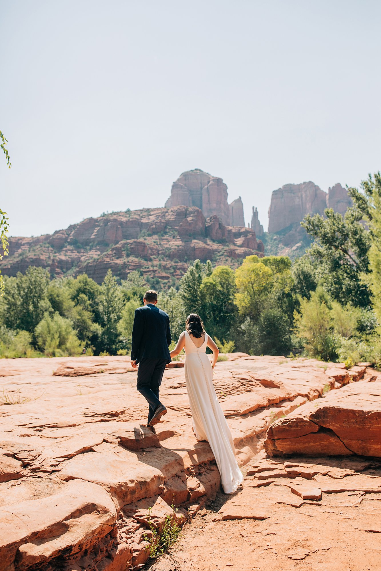 Matthew leads Stephanie through the Sedona landscape, while her long white wedding dress trails behind.