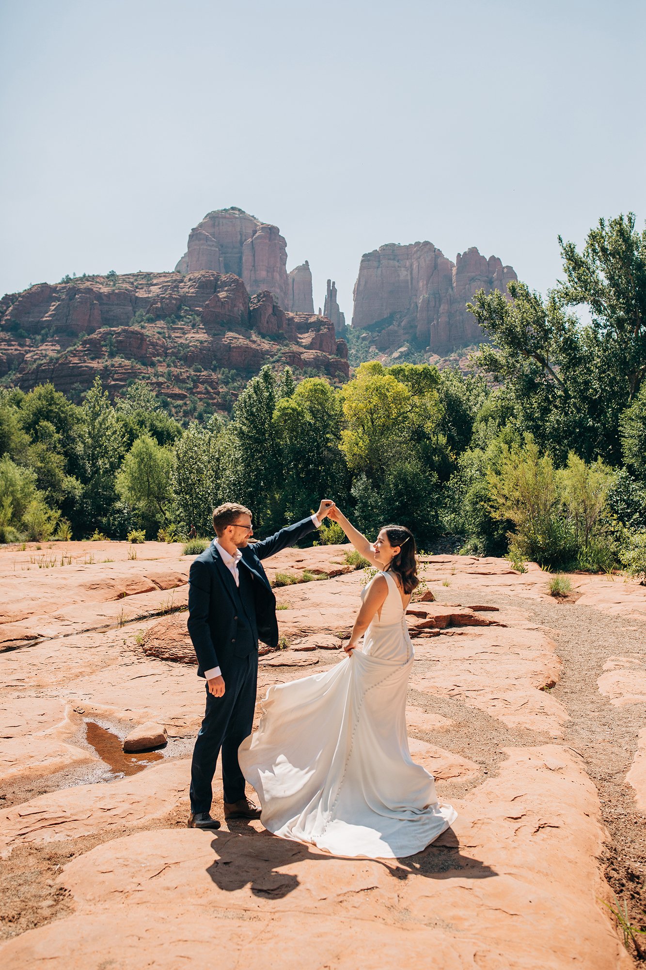 Stephanie and Matthew dance together in their wedding attire, with Sedona cliffs and trees in the background