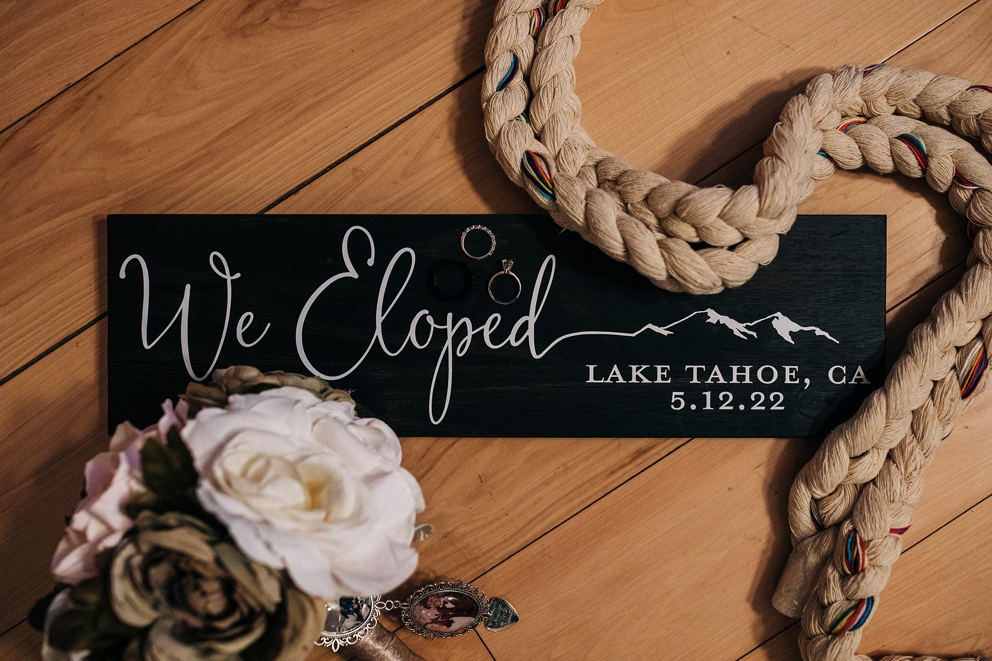 A handfasting cord, wedding rings, and a sign that reads "Eloped in Lake Tahoe, California".