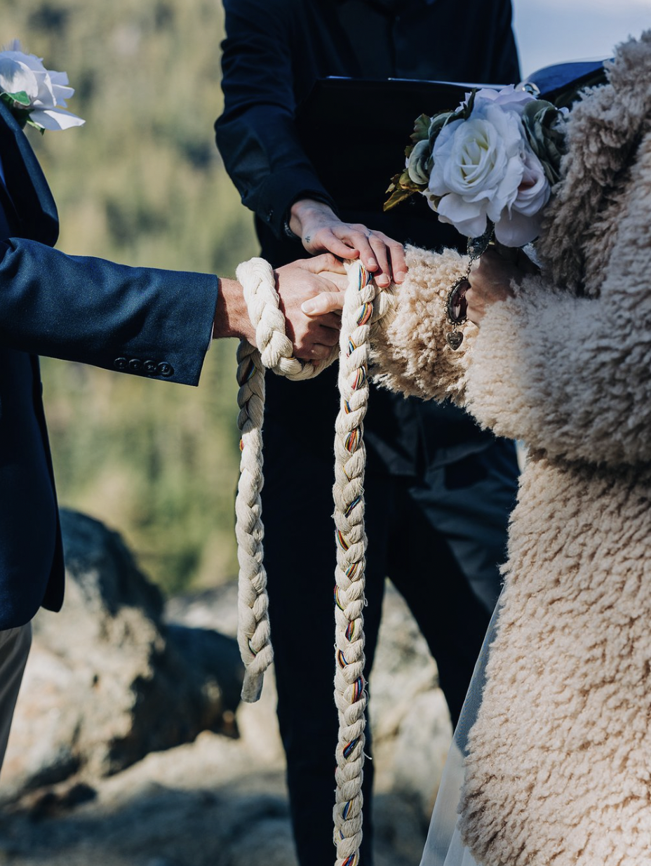 Two hands are bound by a home-made handfasting cord during an elopement.