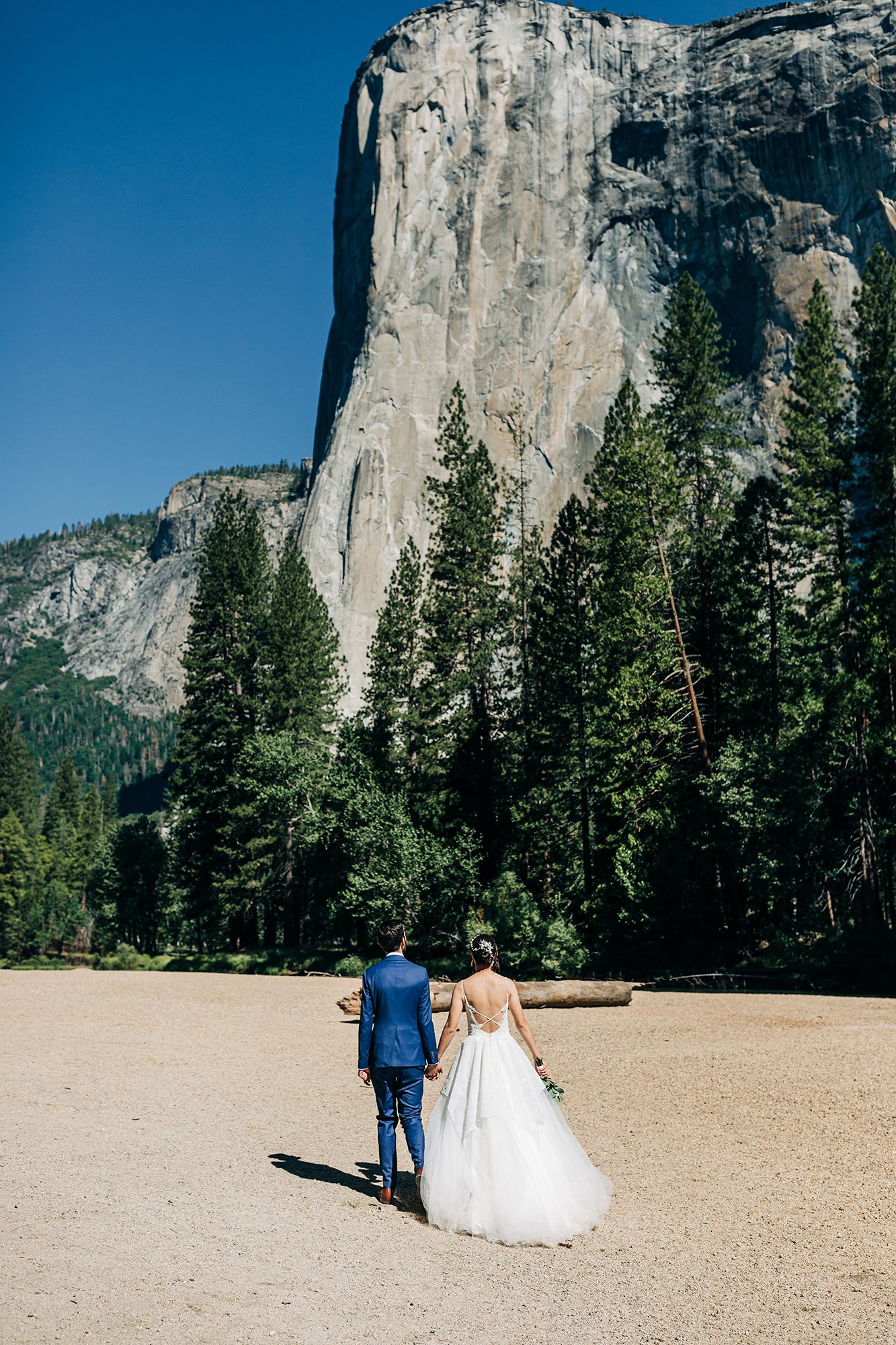 Yooree and Jarrod walk together under El Capitan on their wedding day. 