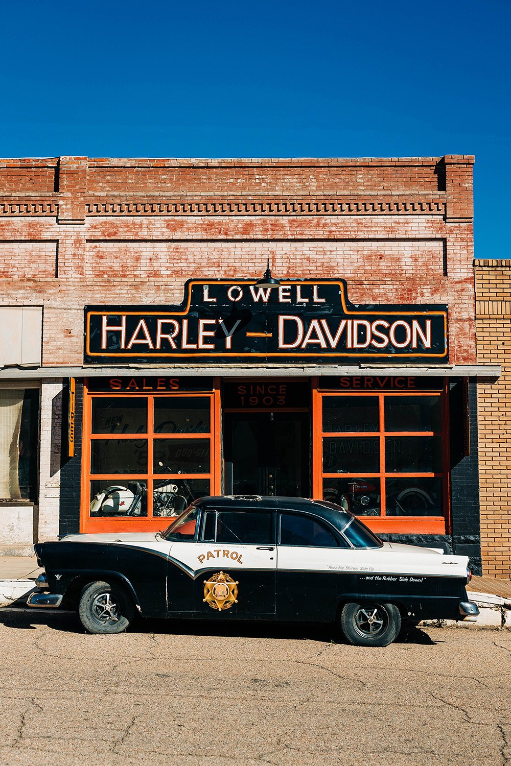 A retro police car in front of a retro Harley-Davidson building.