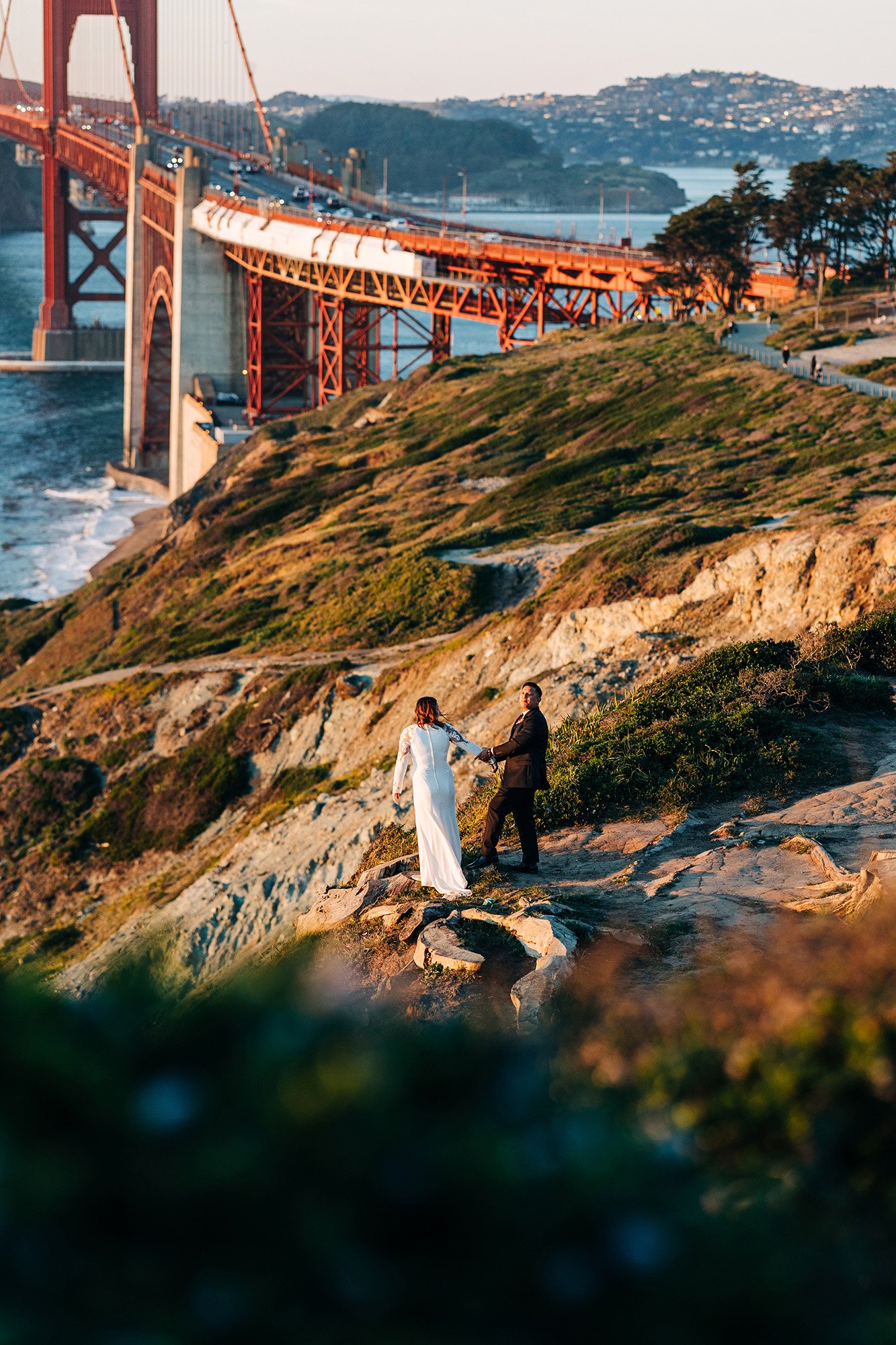 Ashley and Paul stand together on a cliff overlooking the iconic Golden Gate Bridge in San Francisco, California.
