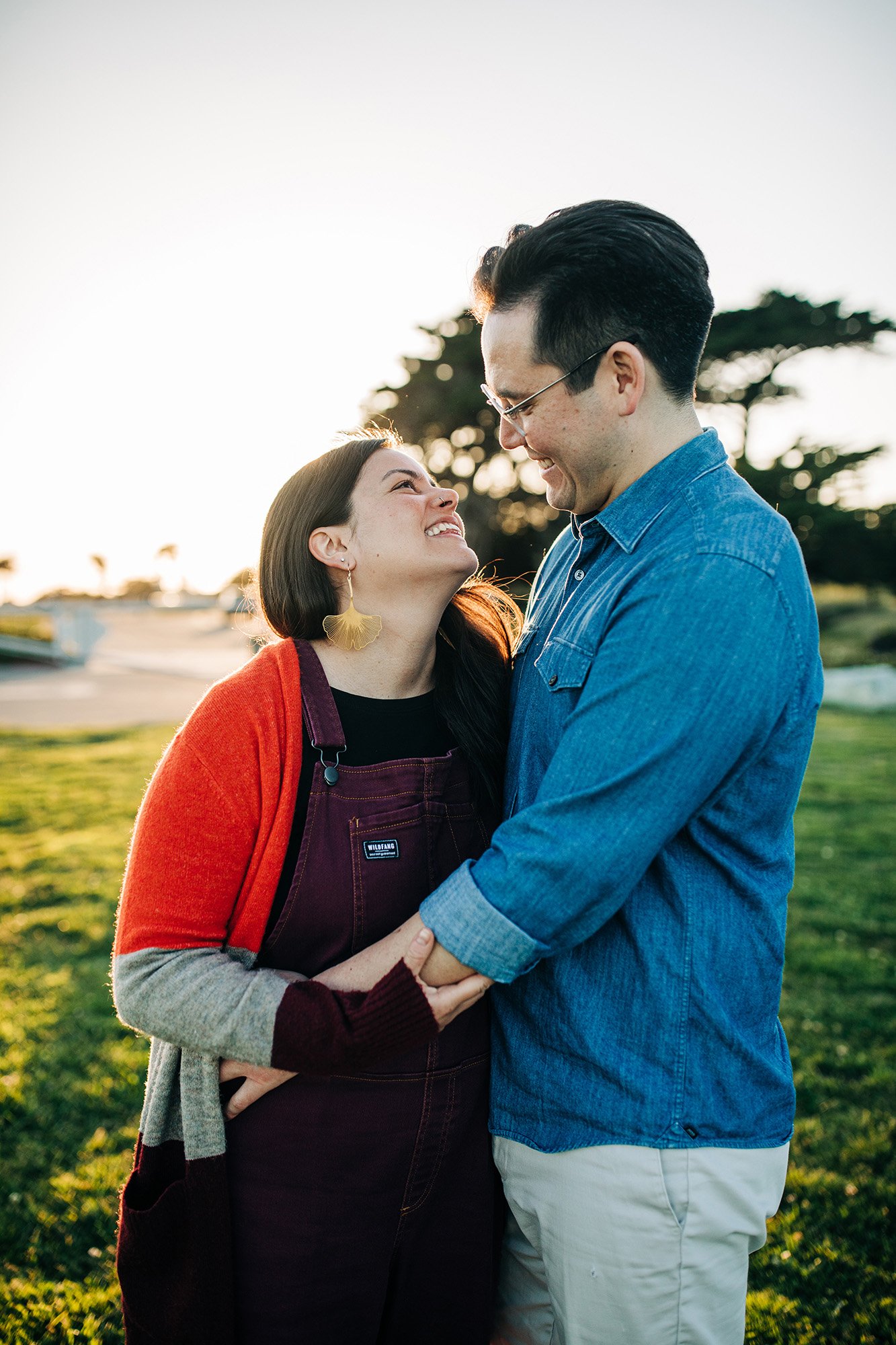 Chloe and Adam cuddle together on the greenery in front of a lighthouse in Santa Cruz, California.