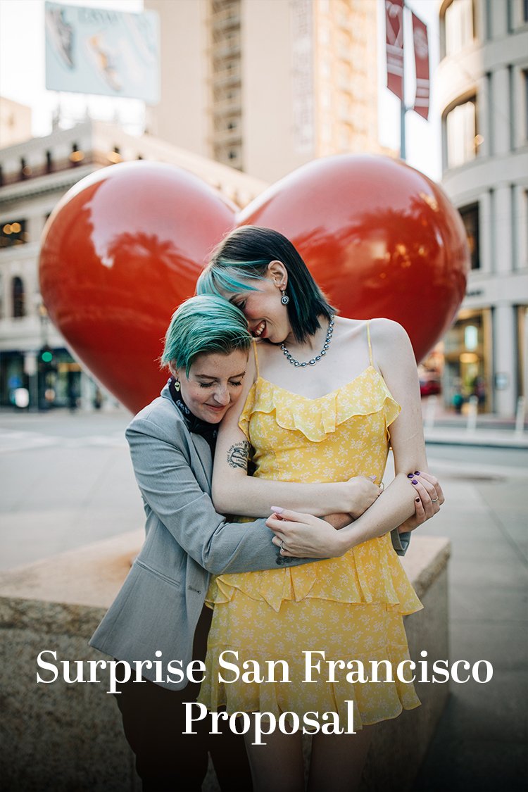 An and Sam cuddle in front of a heart sculpture during their engagement session in San Francisco.