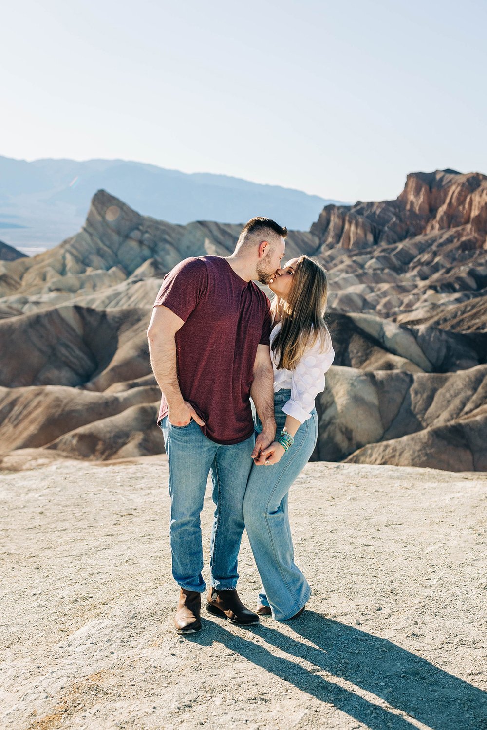 Aly and Alex kiss in front of a desert mountain view in Death Valley National Park.