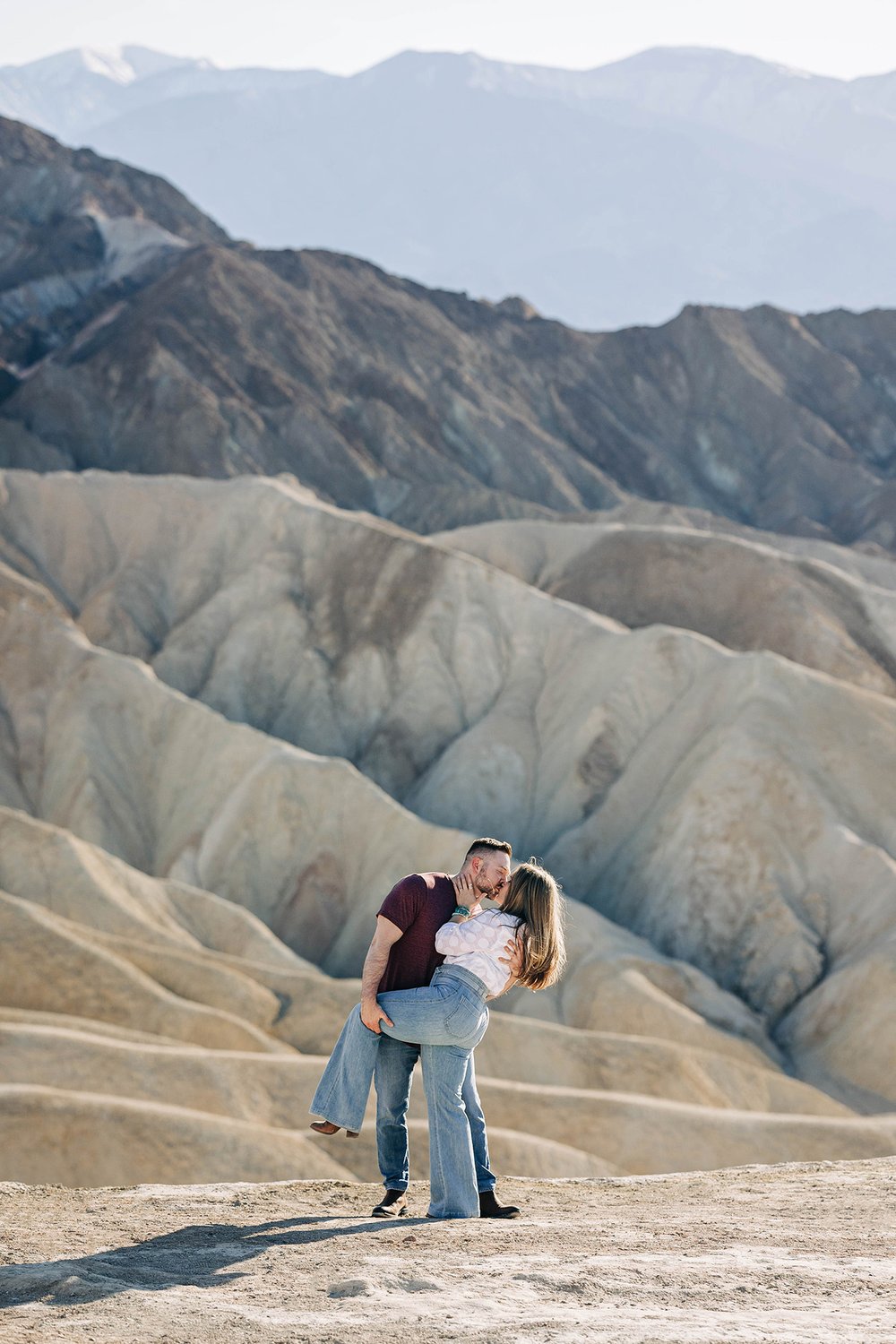 A couple kisses in front of a mountain view.