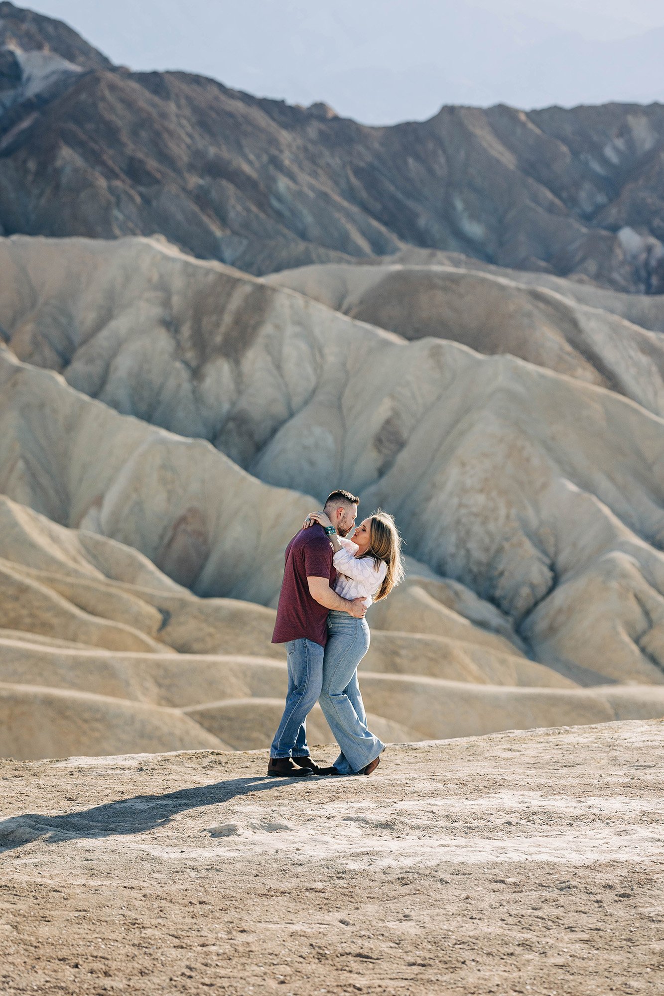 A couple embraces in front of rolling desert mountains.