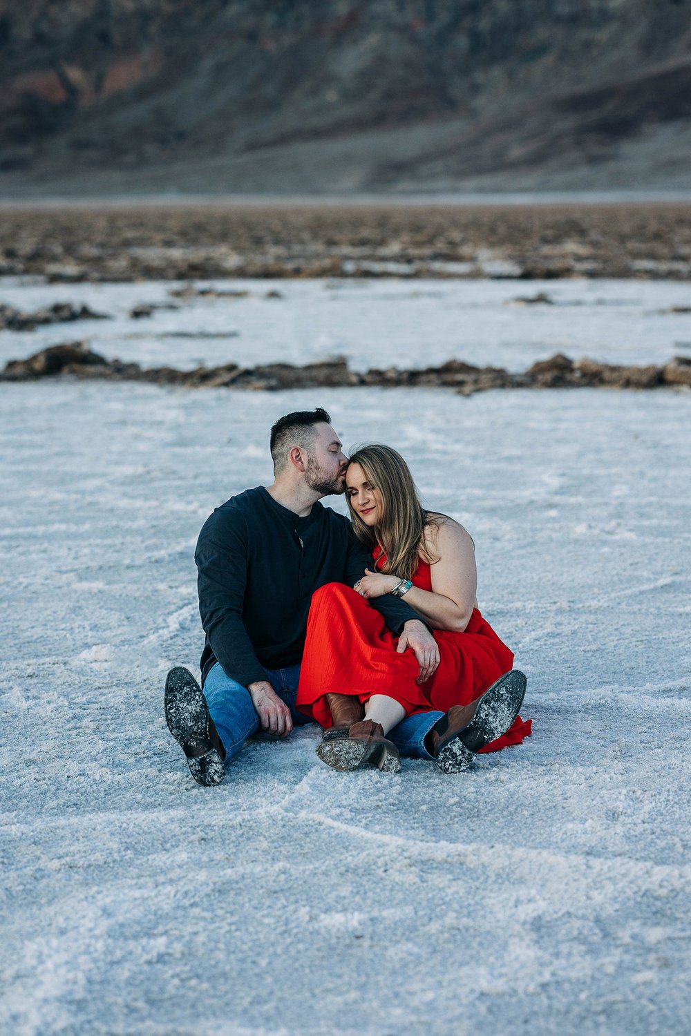 A couple sits together on the salt flats during their engagement session.