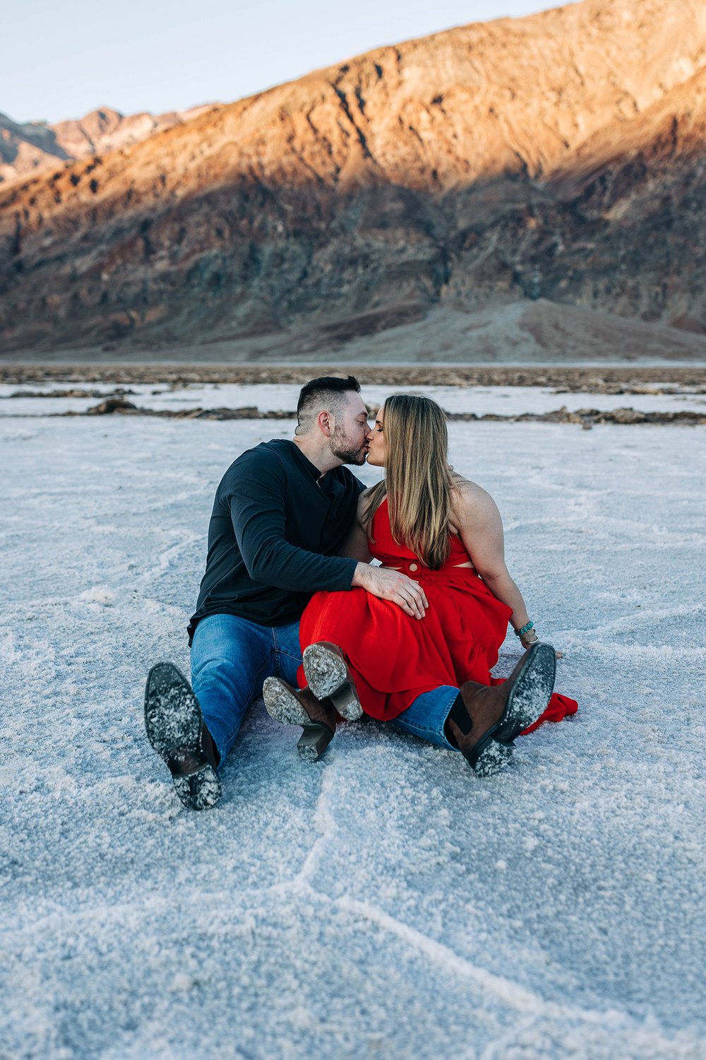 Alex and Aly sit together on the salt flats with a view of the mountains.