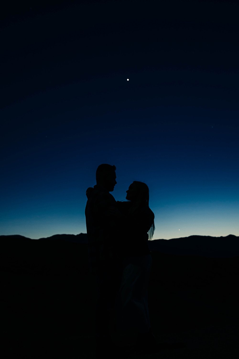 A couple is silhouetted against a starry sky.