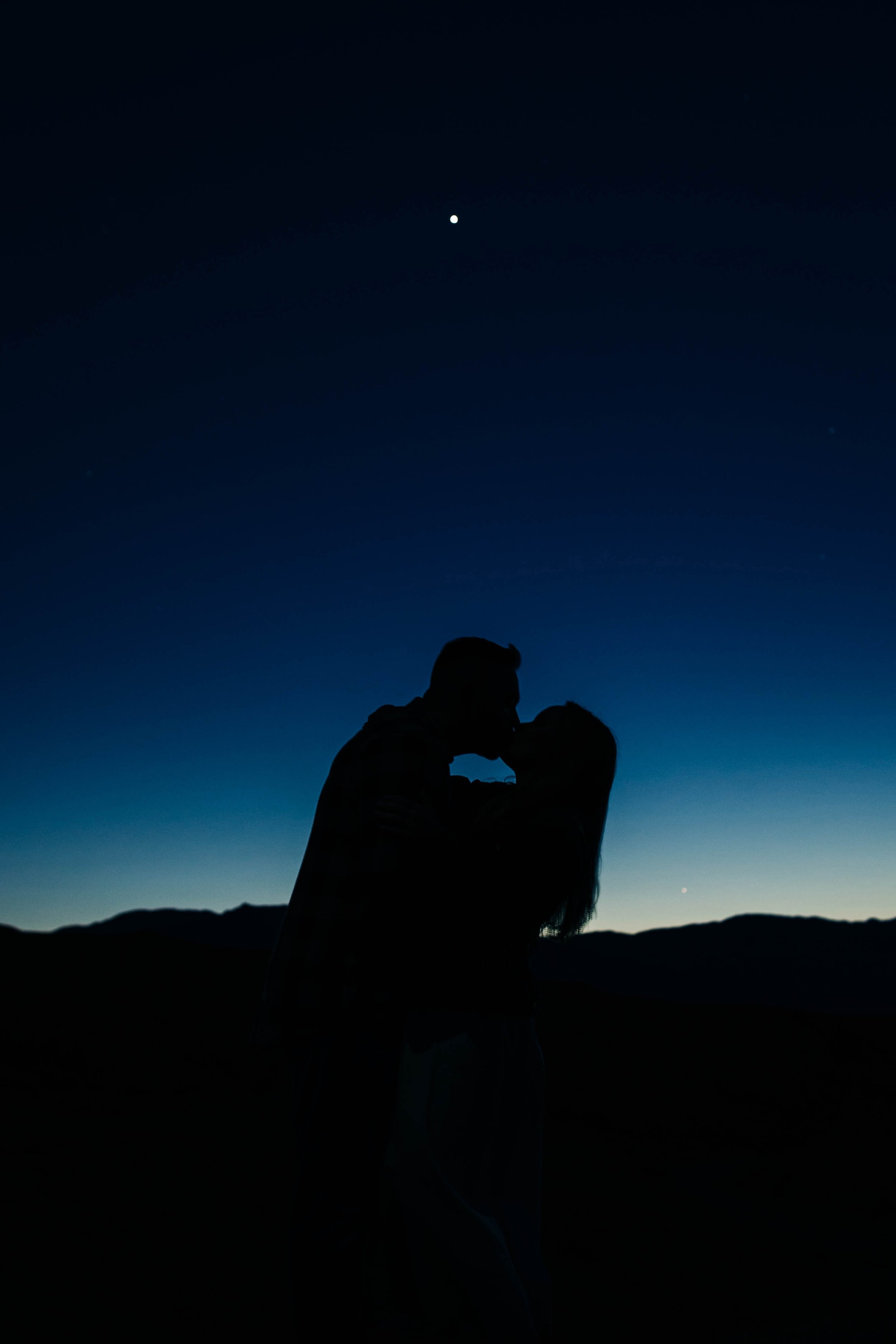 A couple kisses in front of a starry dusk sky.